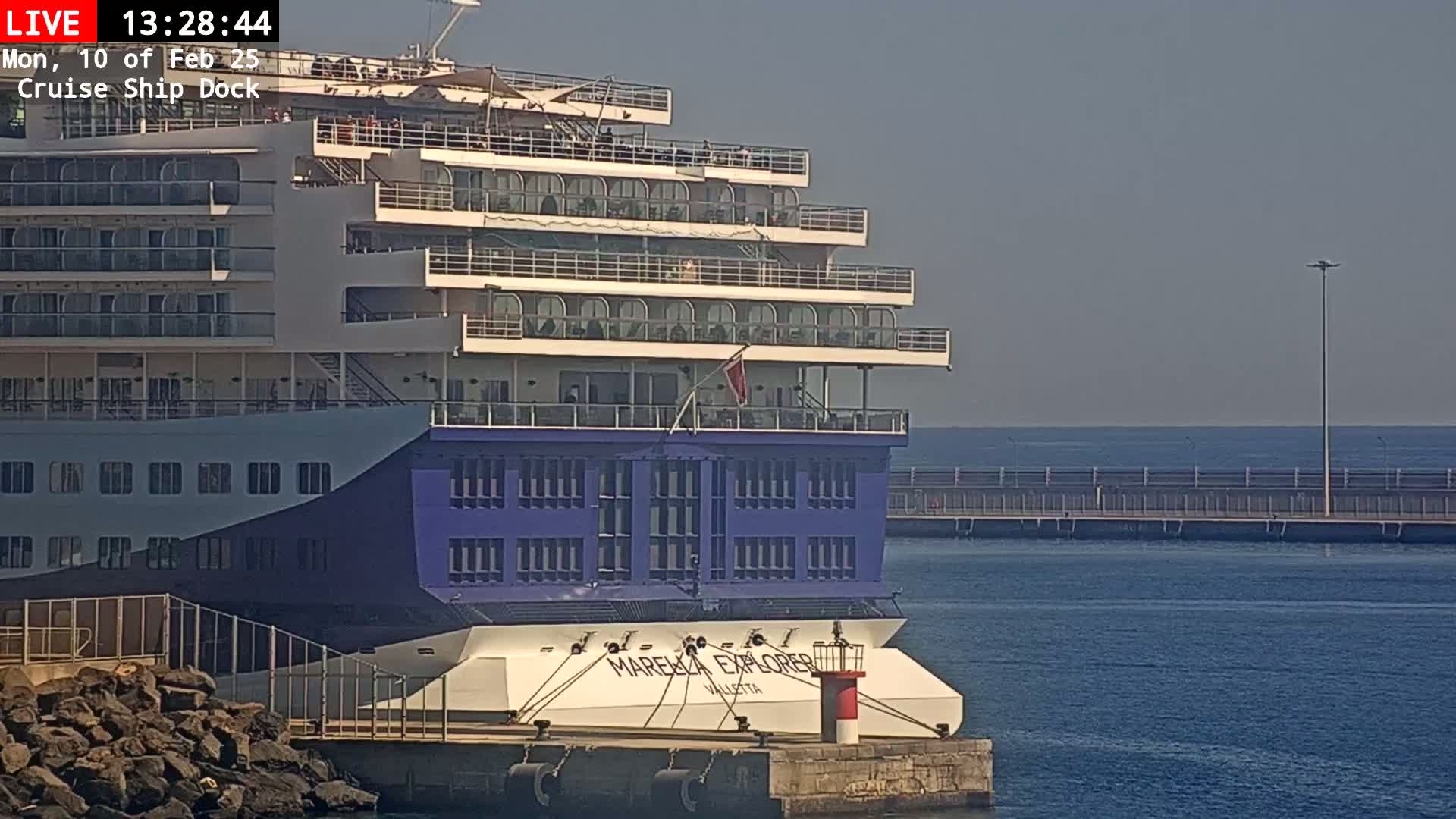 A large cruise ship is docked at a pier on a calm, sunny day.