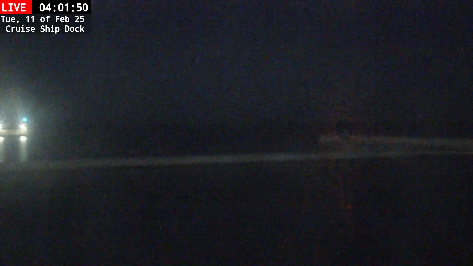 A dark, nighttime view of a body of water, possibly a dock area, with faint lights visible in the distance.