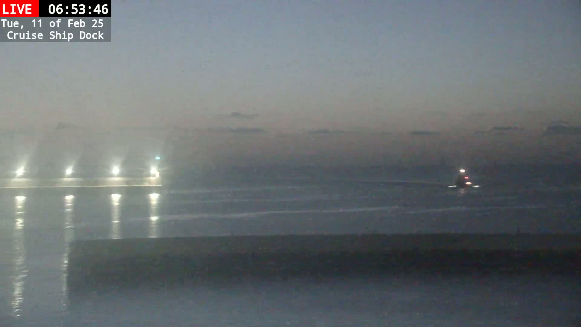 A dimly lit cruise ship dock with a small vessel on the water in the distance under a hazy, twilight sky.