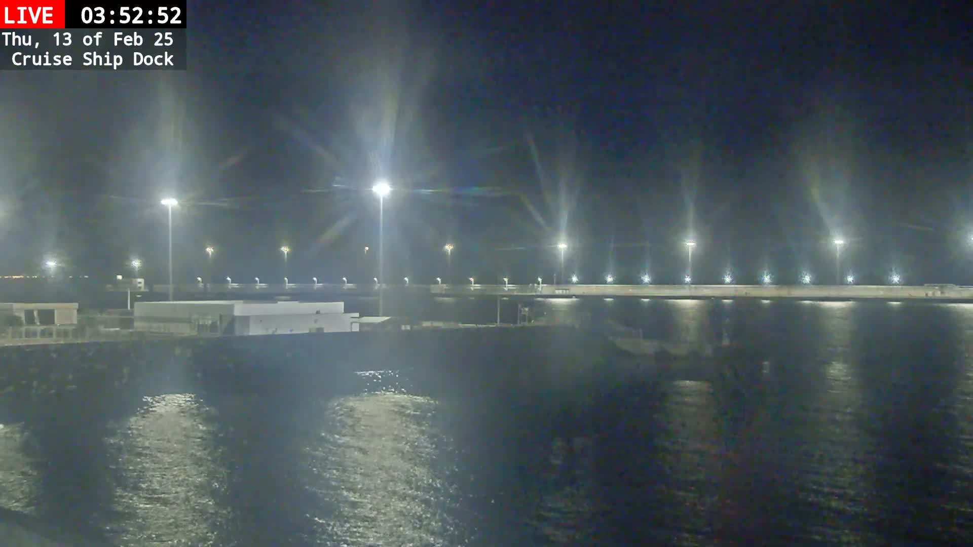 A nighttime view of a cruise ship dock illuminated by bright lights, showing calm water.