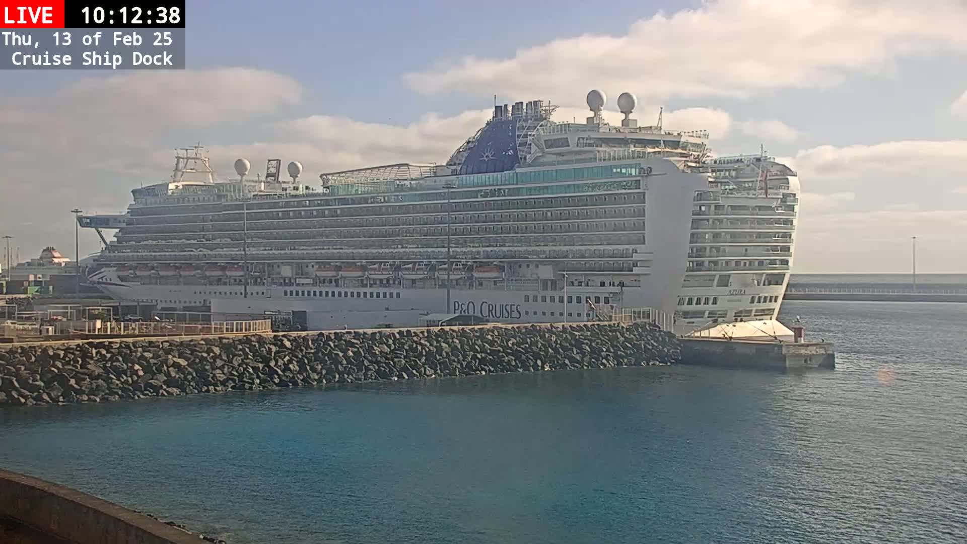 A large cruise ship is docked at a port on a partly cloudy day.