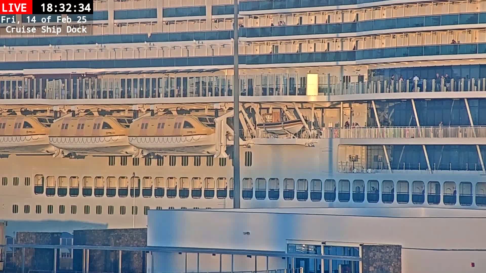A large cruise ship is docked, with several lifeboats visible, under what appears to be a partly sunny sky.