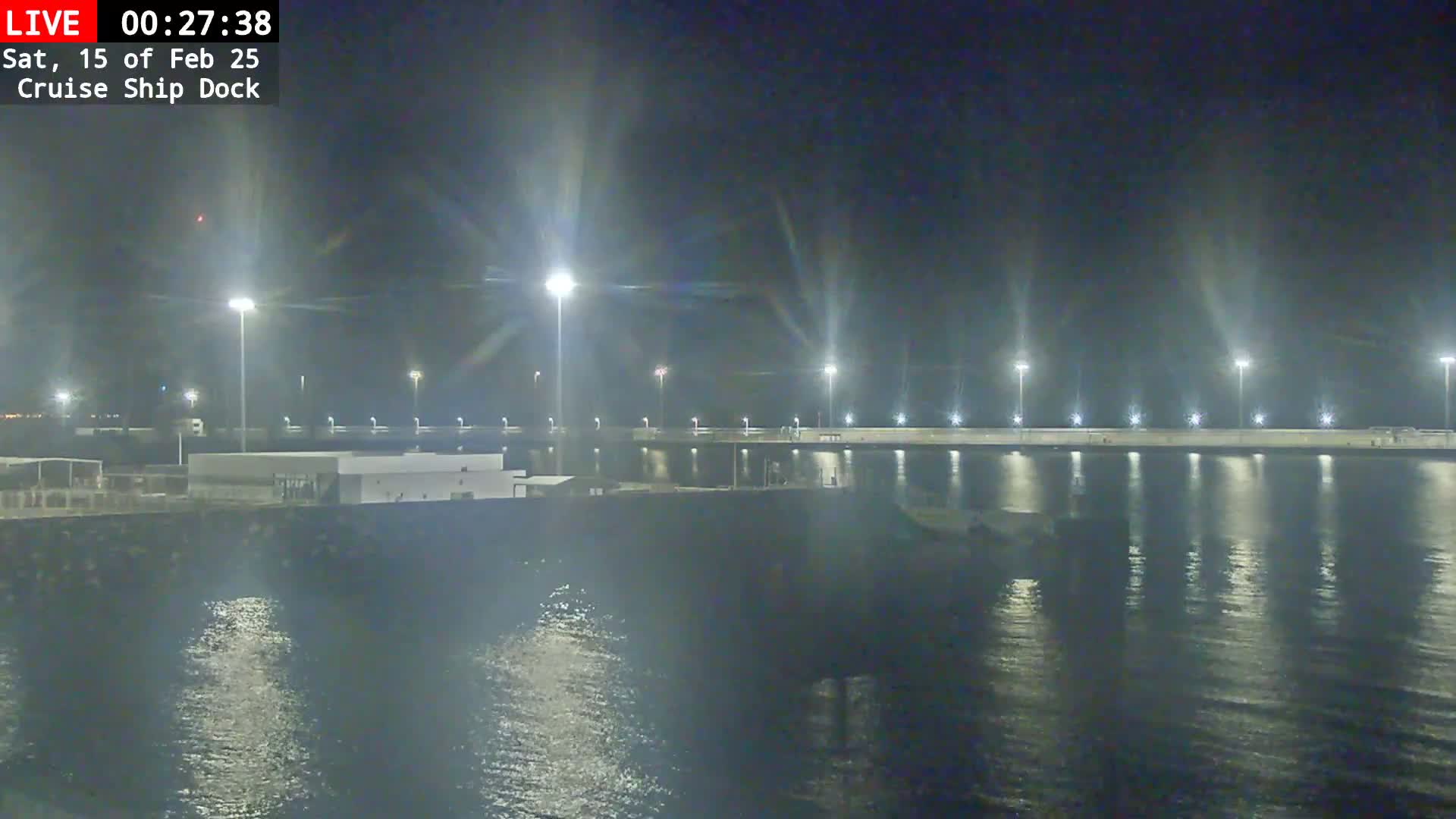 A nighttime view of a brightly lit cruise ship dock and calm water.