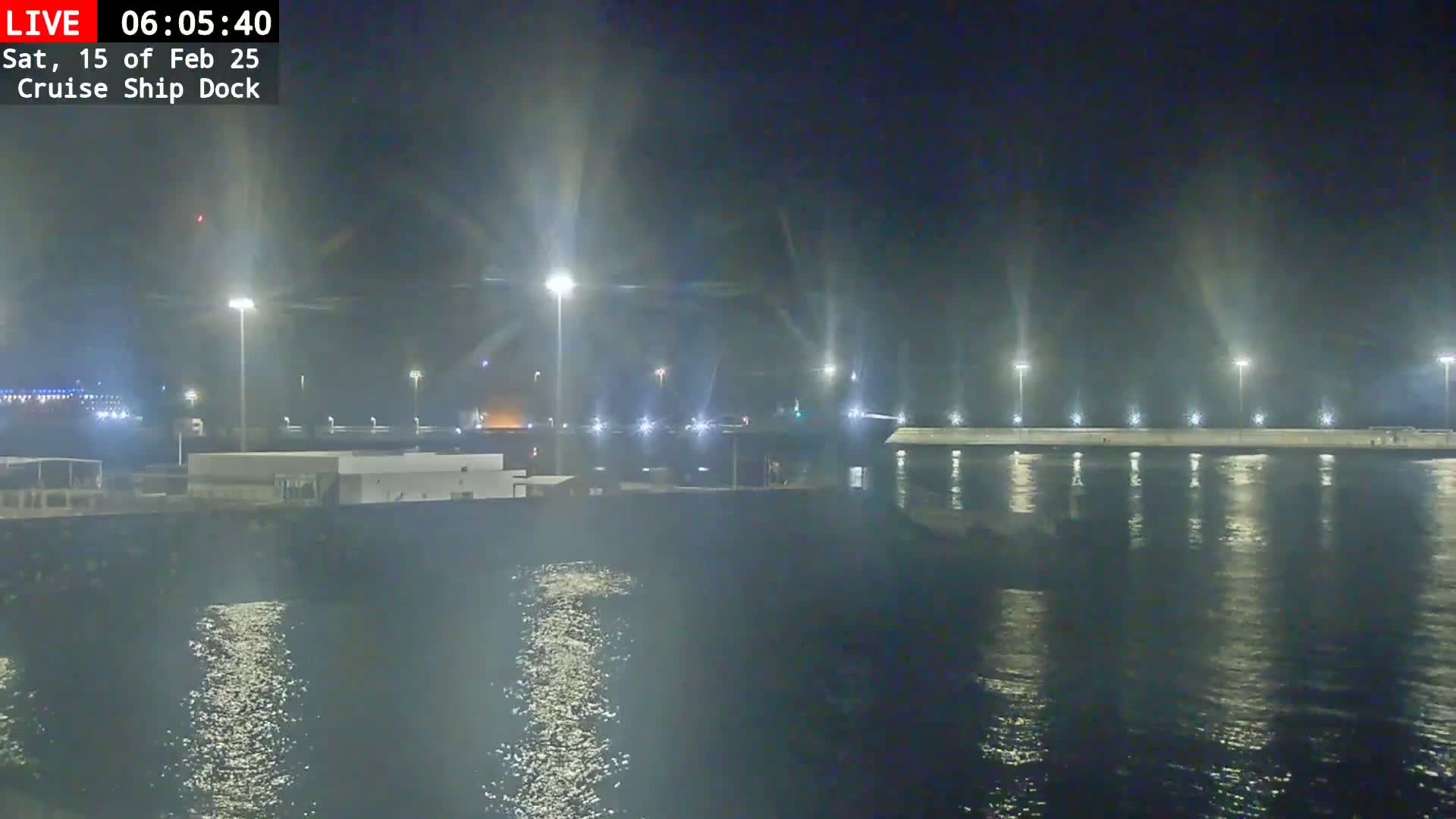 A nighttime view of a cruise ship dock illuminated by bright lights, reflecting on calm water.