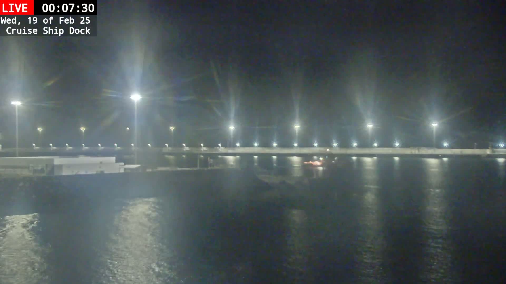 A nighttime view of a cruise ship dock, illuminated by numerous lights, with calm water reflecting the lights.