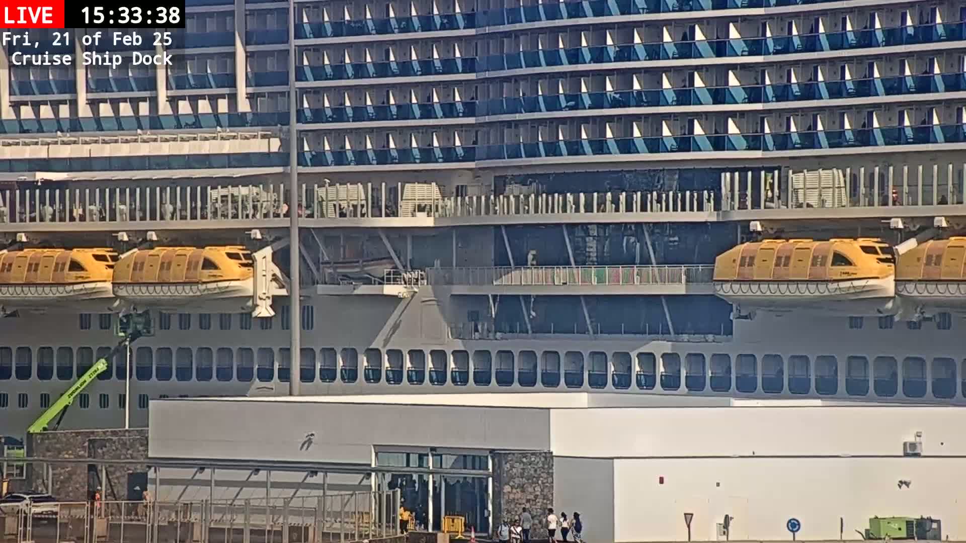 A large cruise ship is docked, with its lifeboats lowered, on a sunny day.