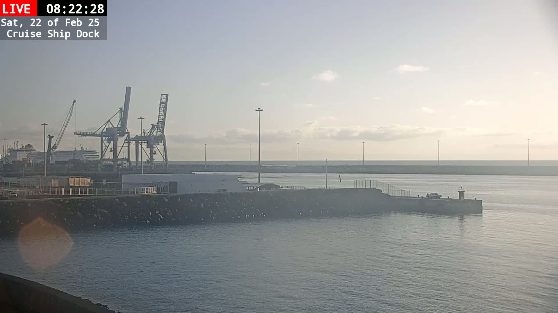 A cruise ship dock with several cranes and a ship is visible under a mostly clear, hazy sky.