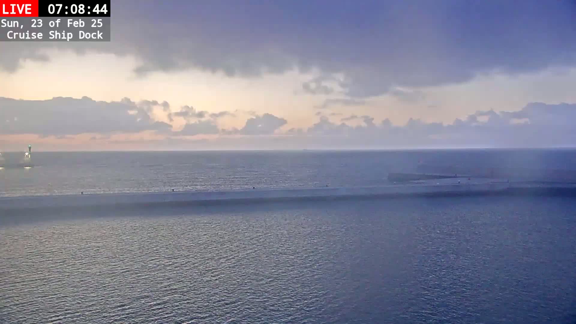 A calm body of water is seen at dawn under a mostly cloudy sky, with a long, thin strip of land separating the water into two sections.