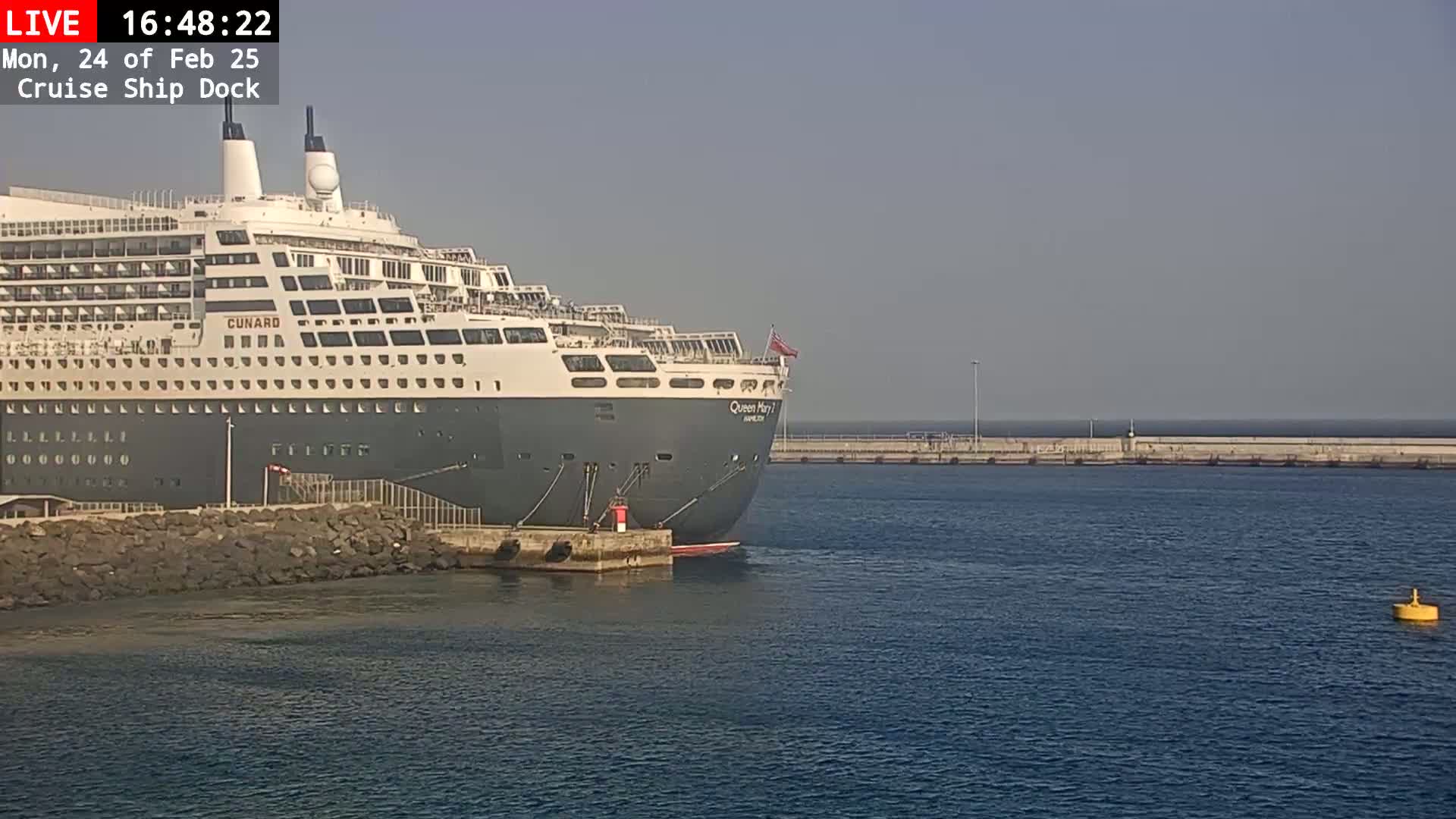 A large cruise ship is docked at a pier on a calm, sunny day.