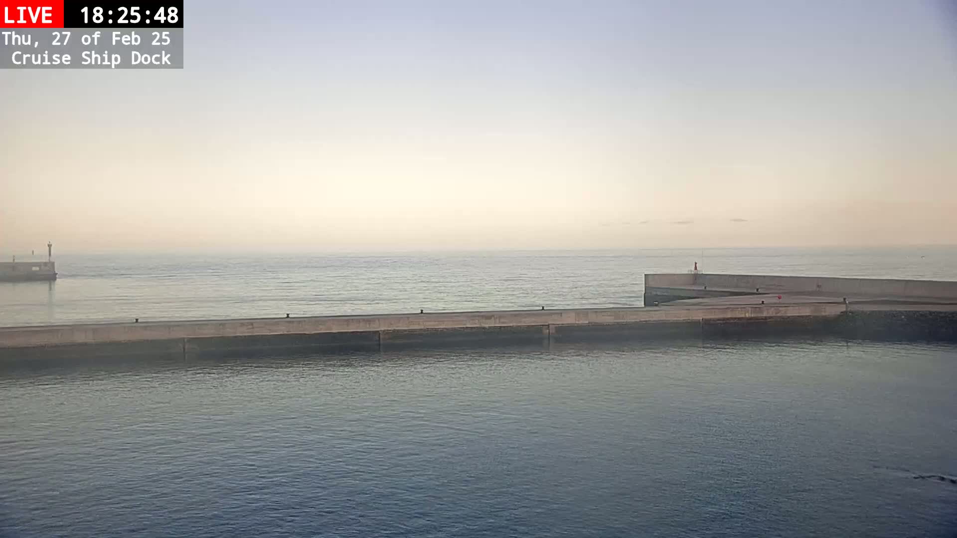 A hazy, calm ocean is seen from above a concrete cruise ship dock.