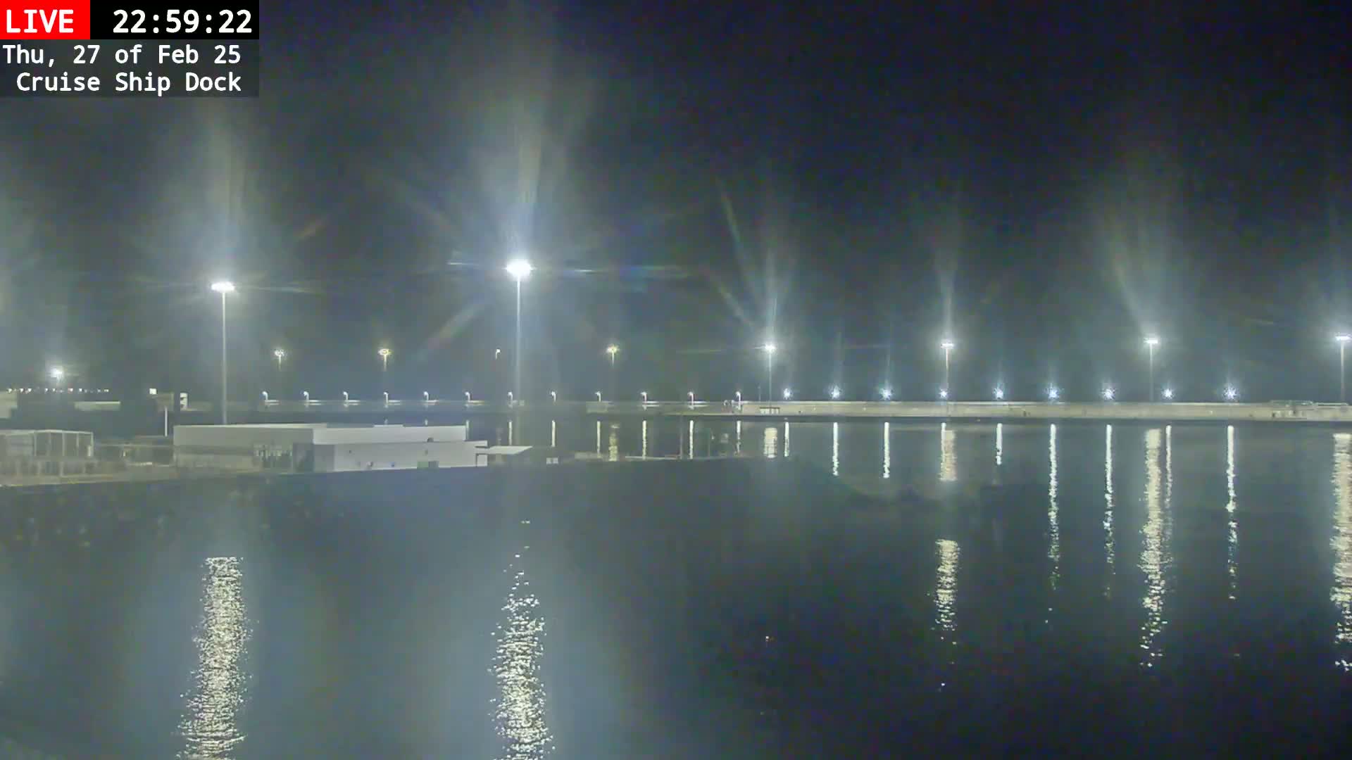 A nighttime view of a cruise ship dock illuminated by bright lights reflecting on calm water.