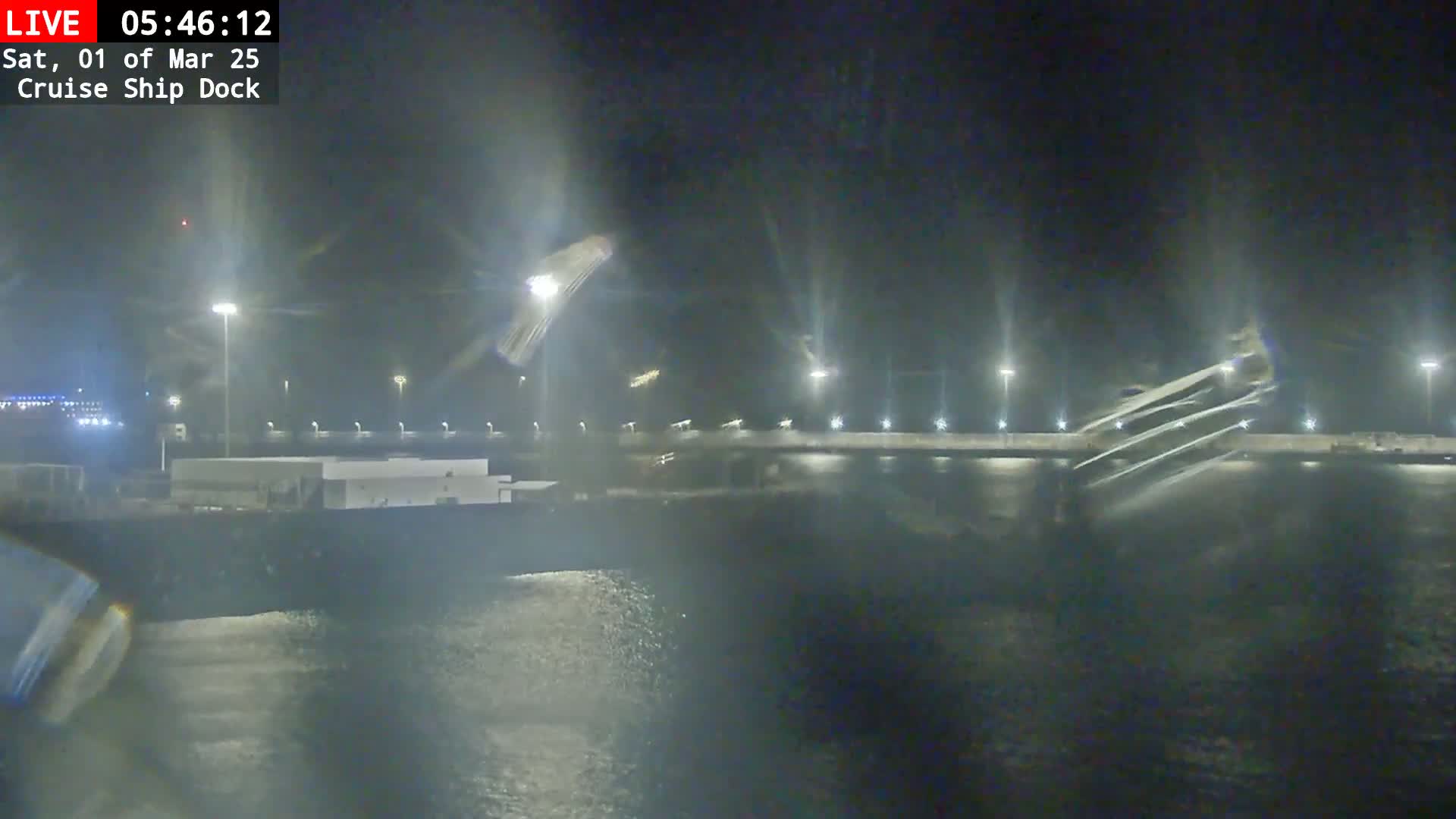A nighttime, blurry view shows a cruise ship docked at a pier with choppy water.