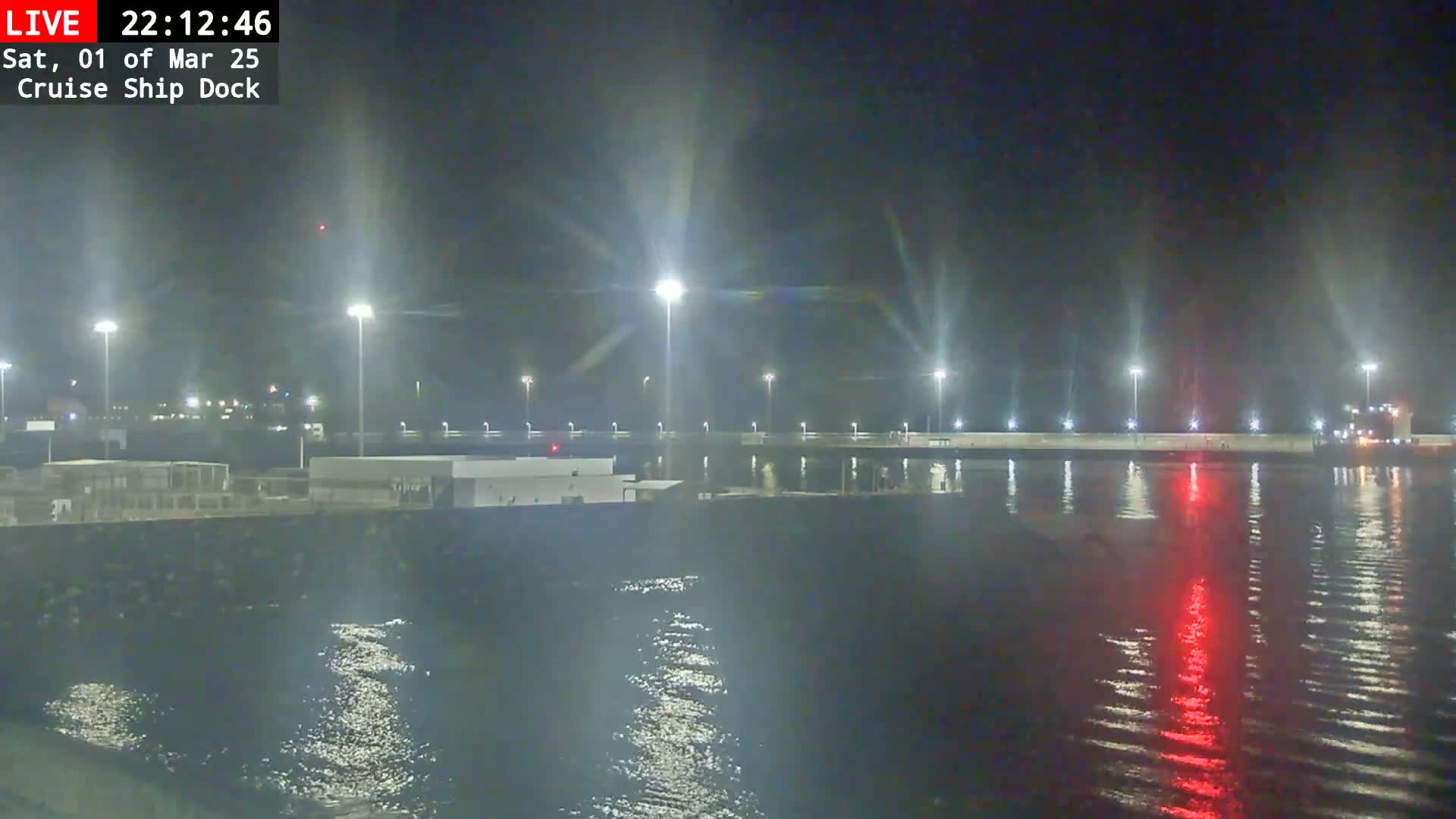 A nighttime view of a cruise ship dock, brightly lit, with calm water reflecting the lights.