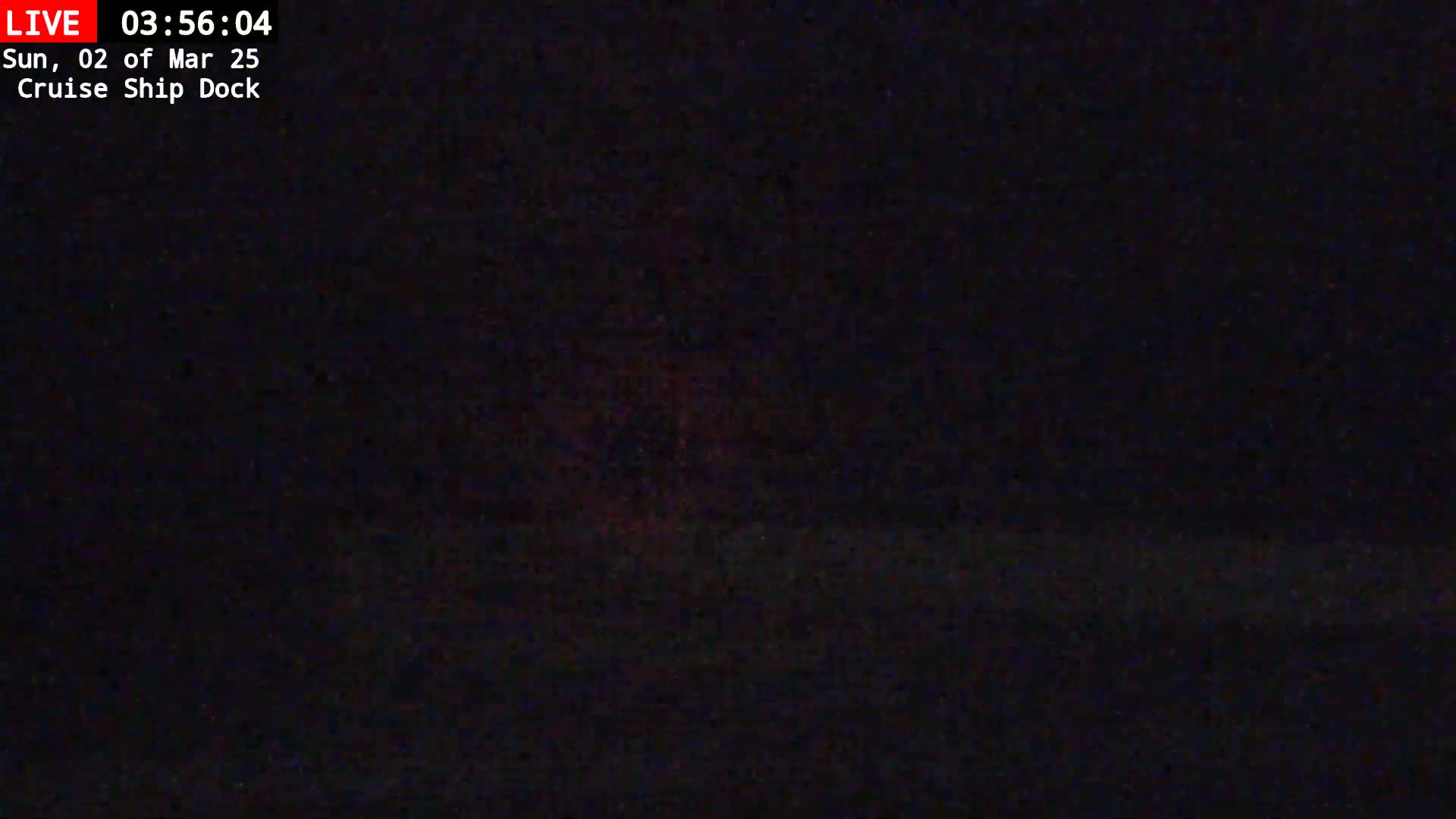 A dark, nighttime scene shows a mostly black view with a faint, reddish glow near the horizon.