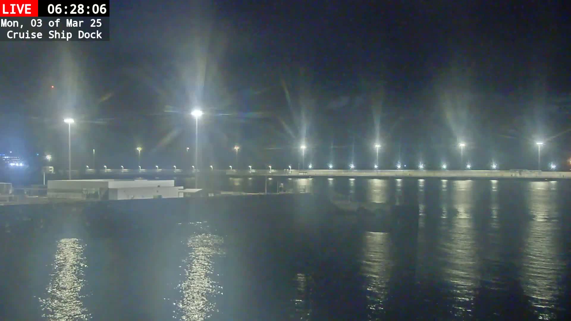 A brightly lit cruise ship dock at night, reflecting in calm water.
