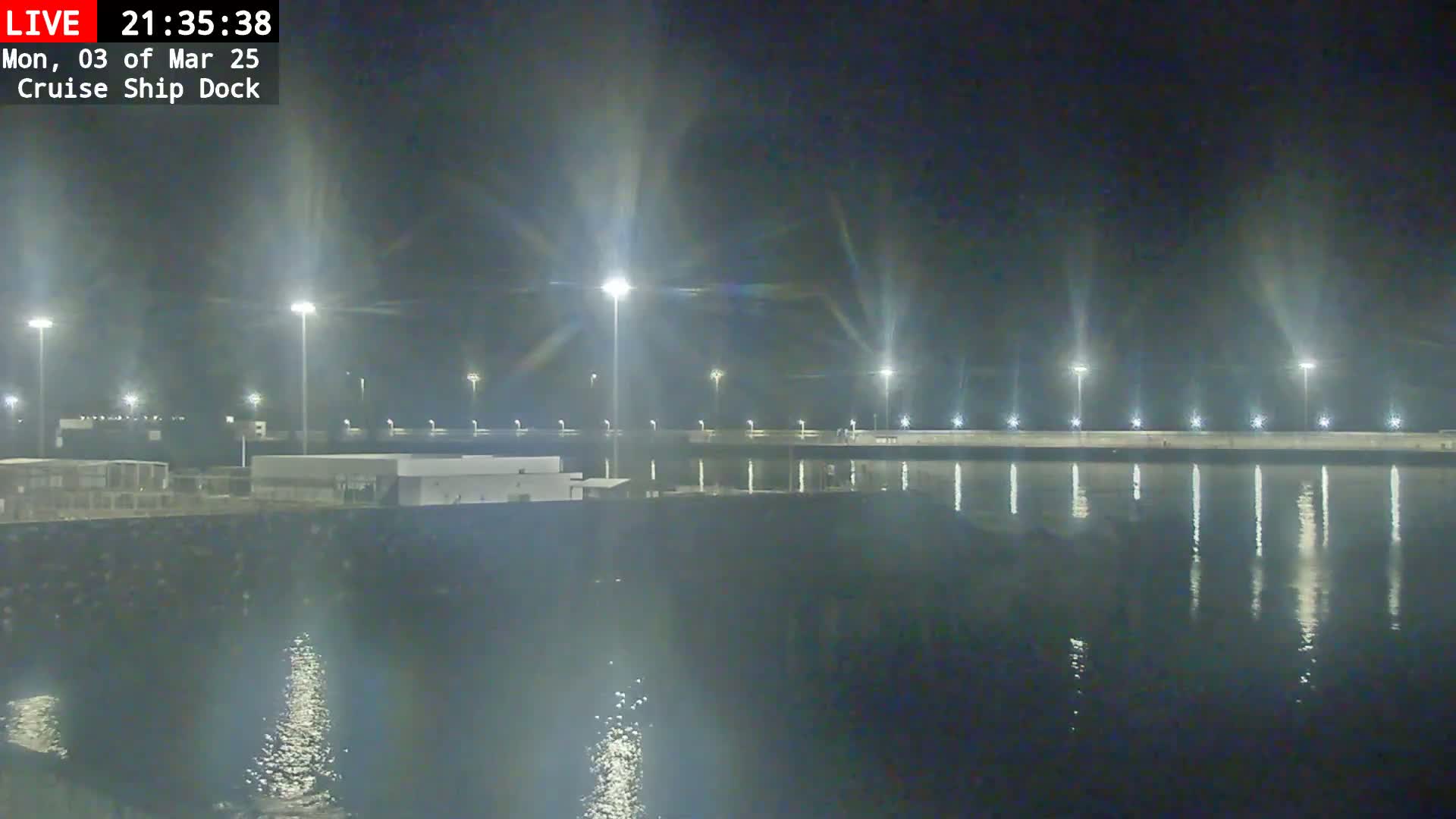 A nighttime view of a cruise ship dock illuminated by bright lights, reflecting on calm water.