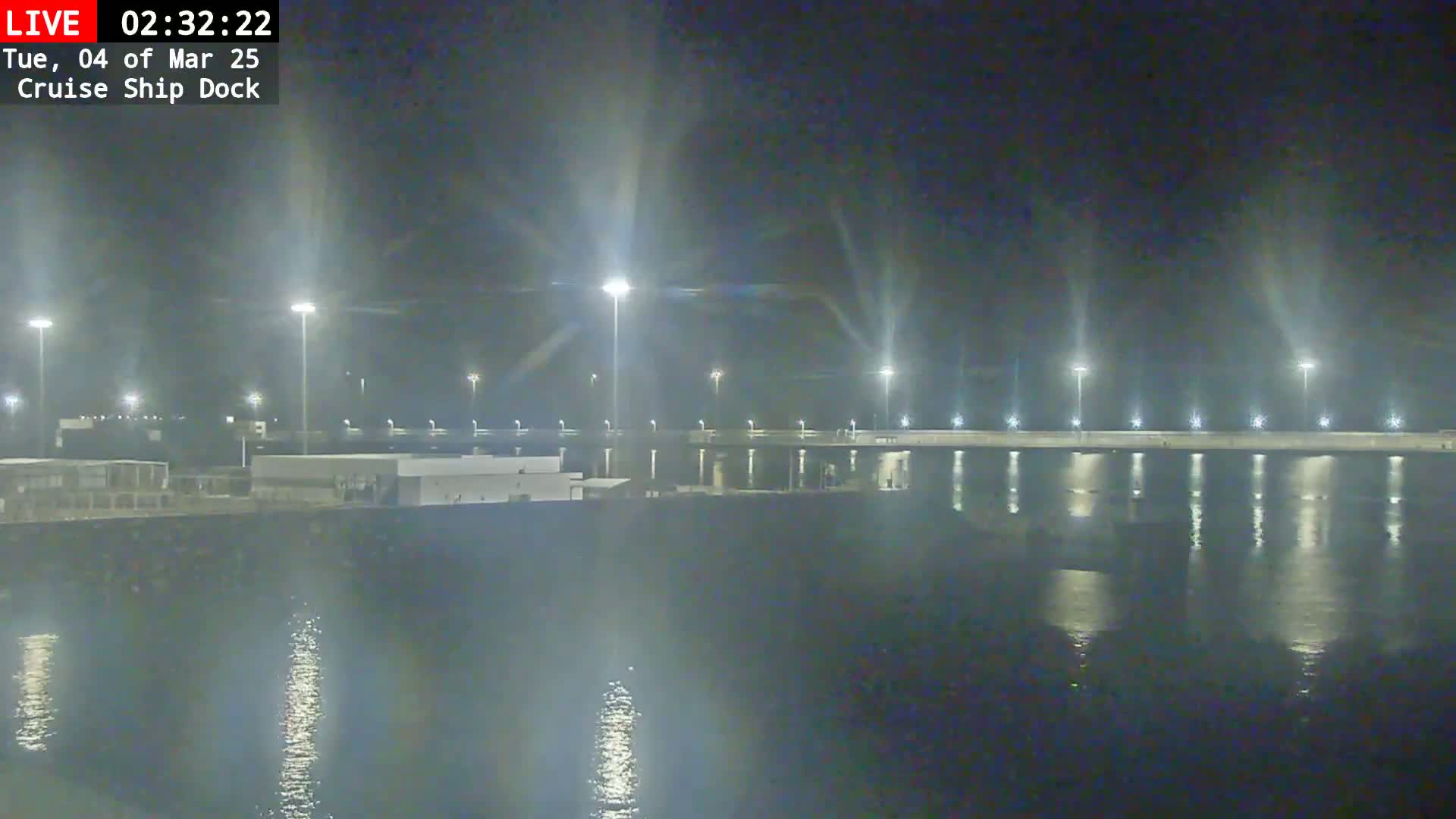A nighttime view of a cruise ship dock illuminated by bright lights, reflecting on calm water.