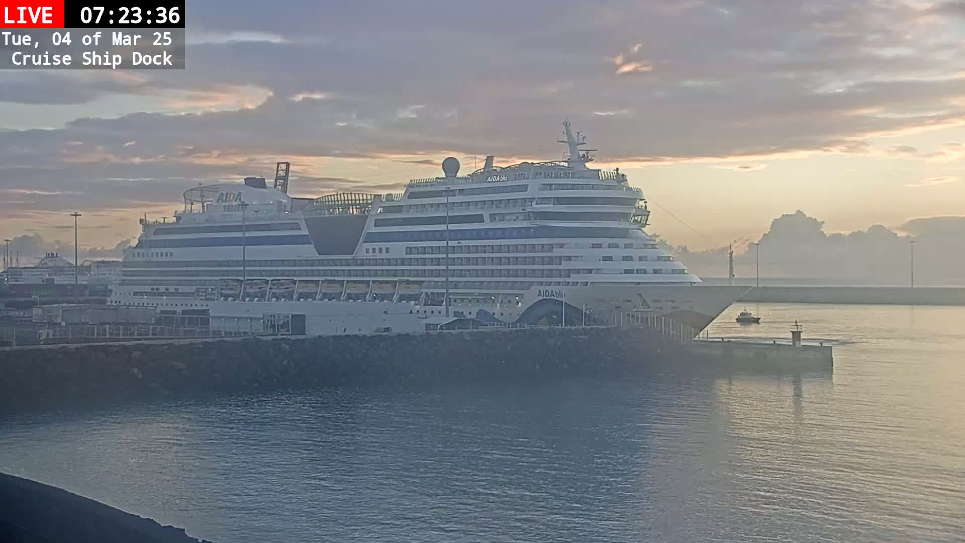 A large cruise ship is docked at sunrise under a hazy, pale sky.