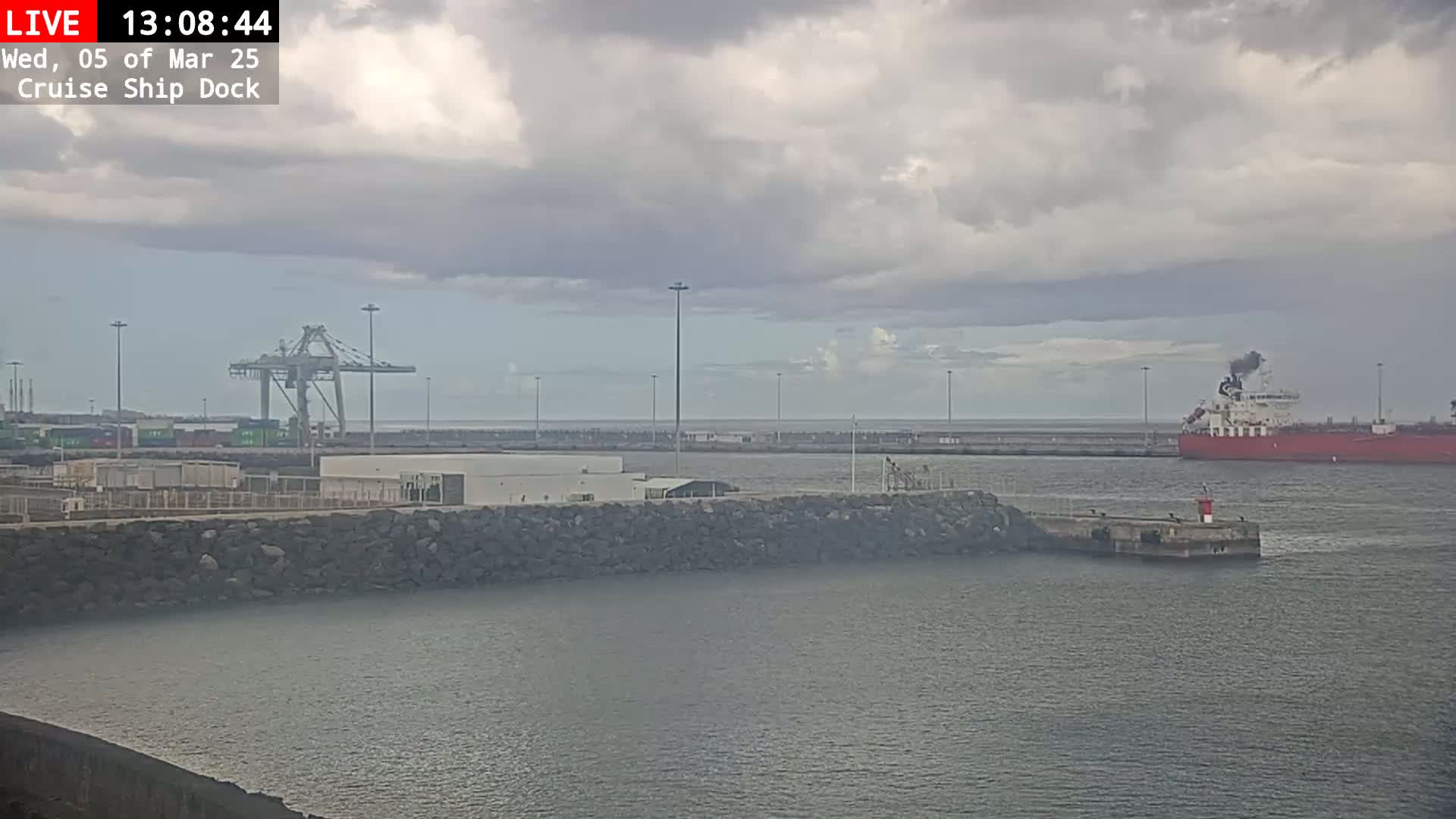 A large cargo ship is docked near a harbor with a crane and overcast skies.