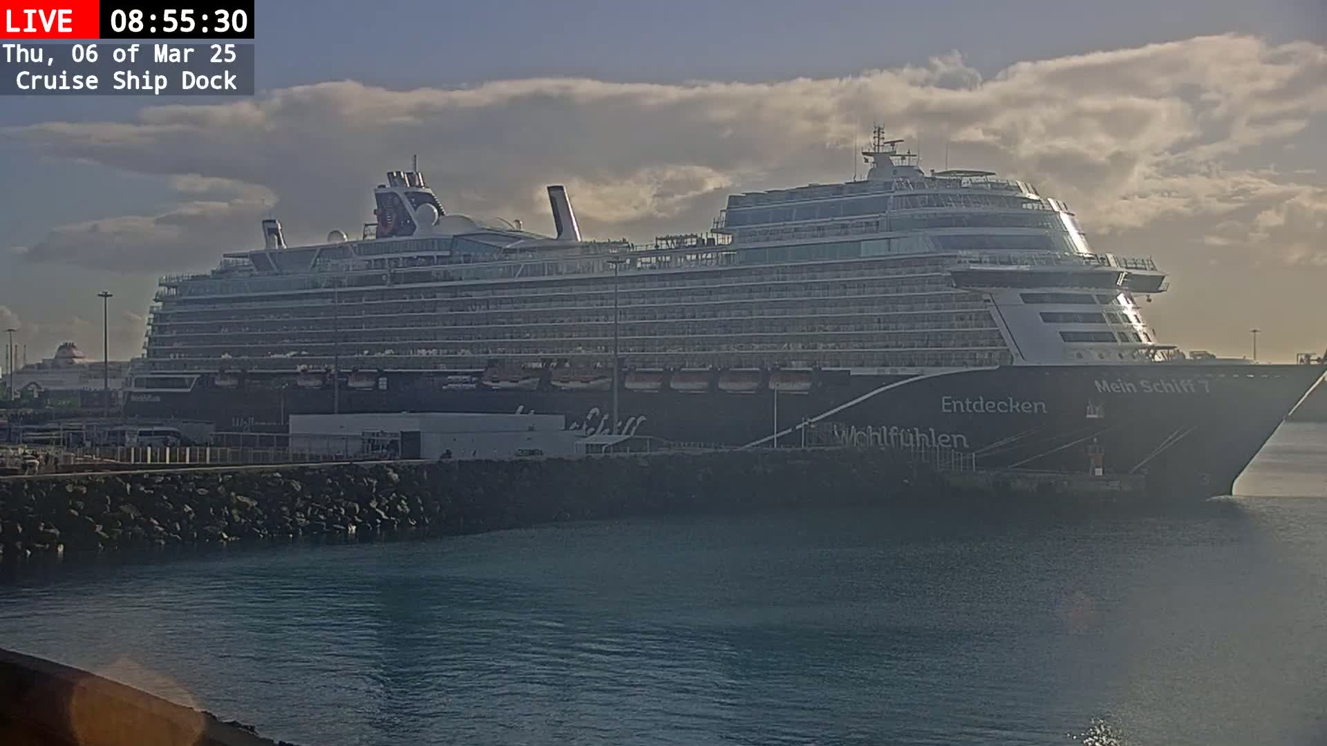 A large cruise ship is docked at a port under a partly cloudy sky.