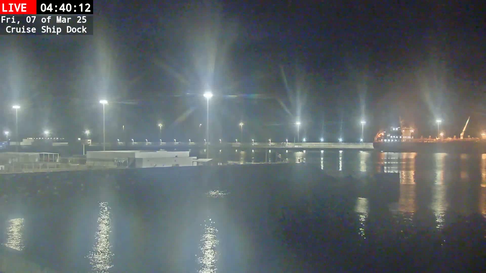 A large ship is docked at a brightly lit cruise ship dock at night.