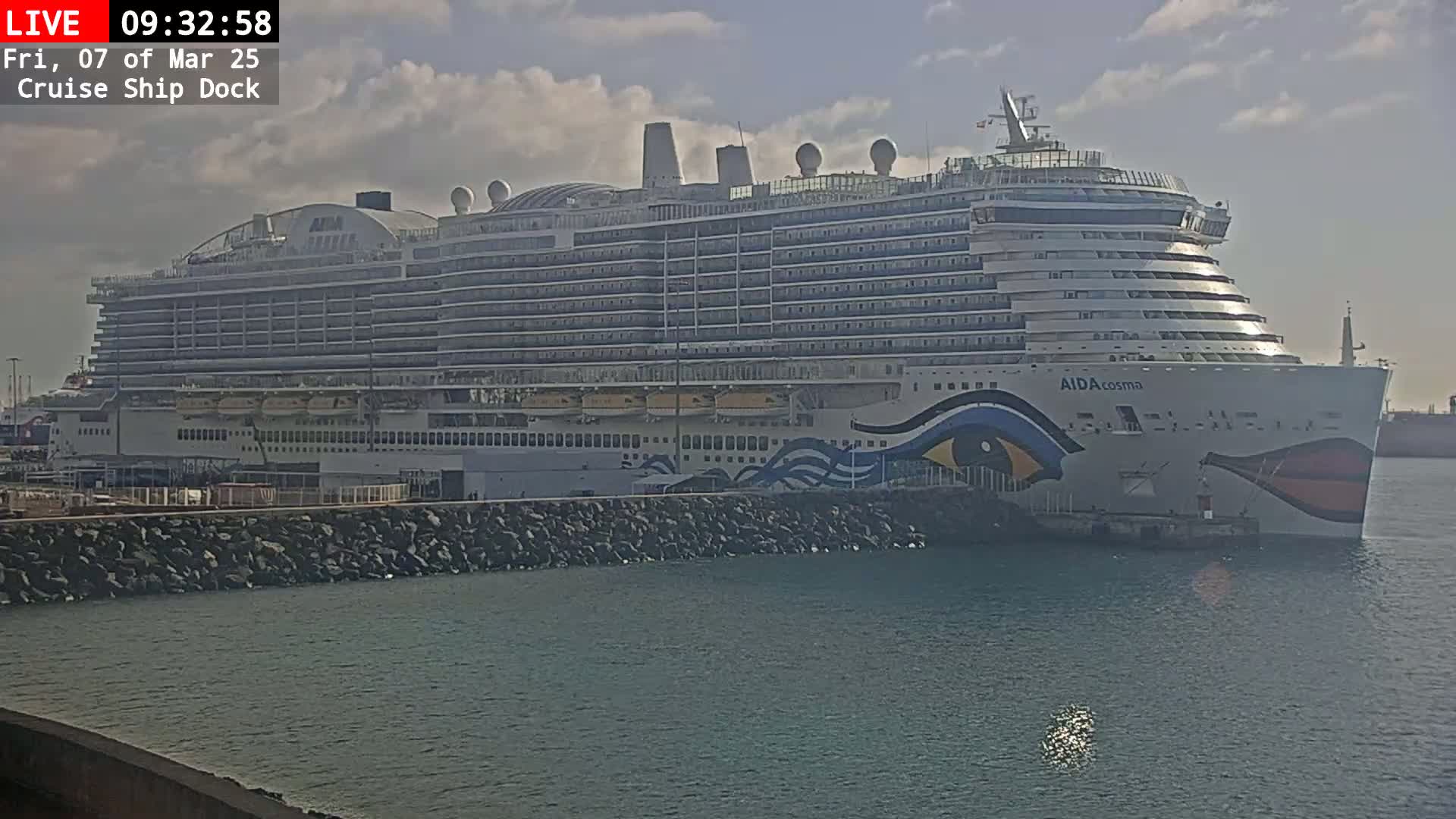 A large cruise ship is docked at a pier on a partly cloudy day.