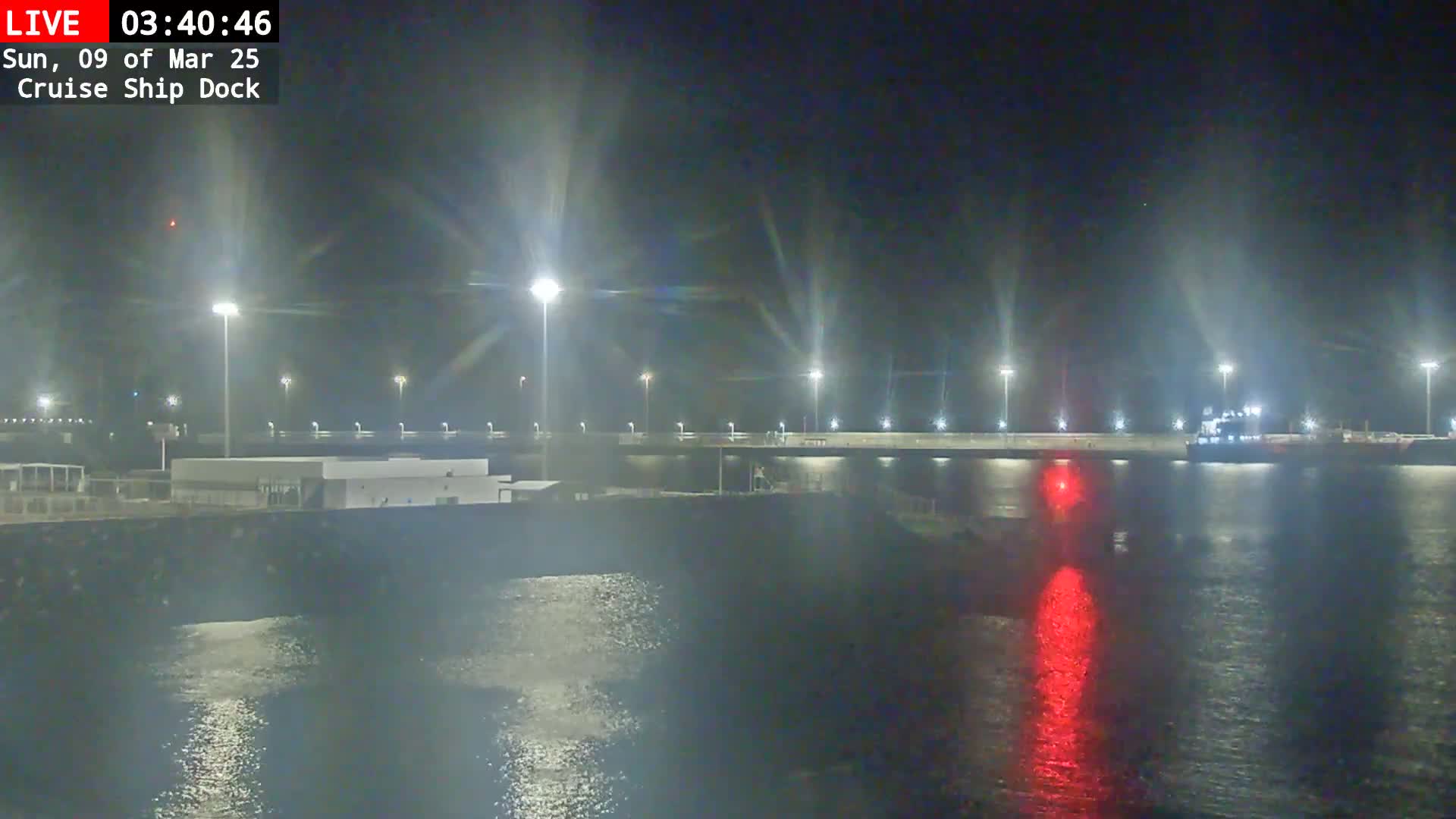 A cruise ship dock at night, illuminated by bright lights, with a large ship visible in the water.