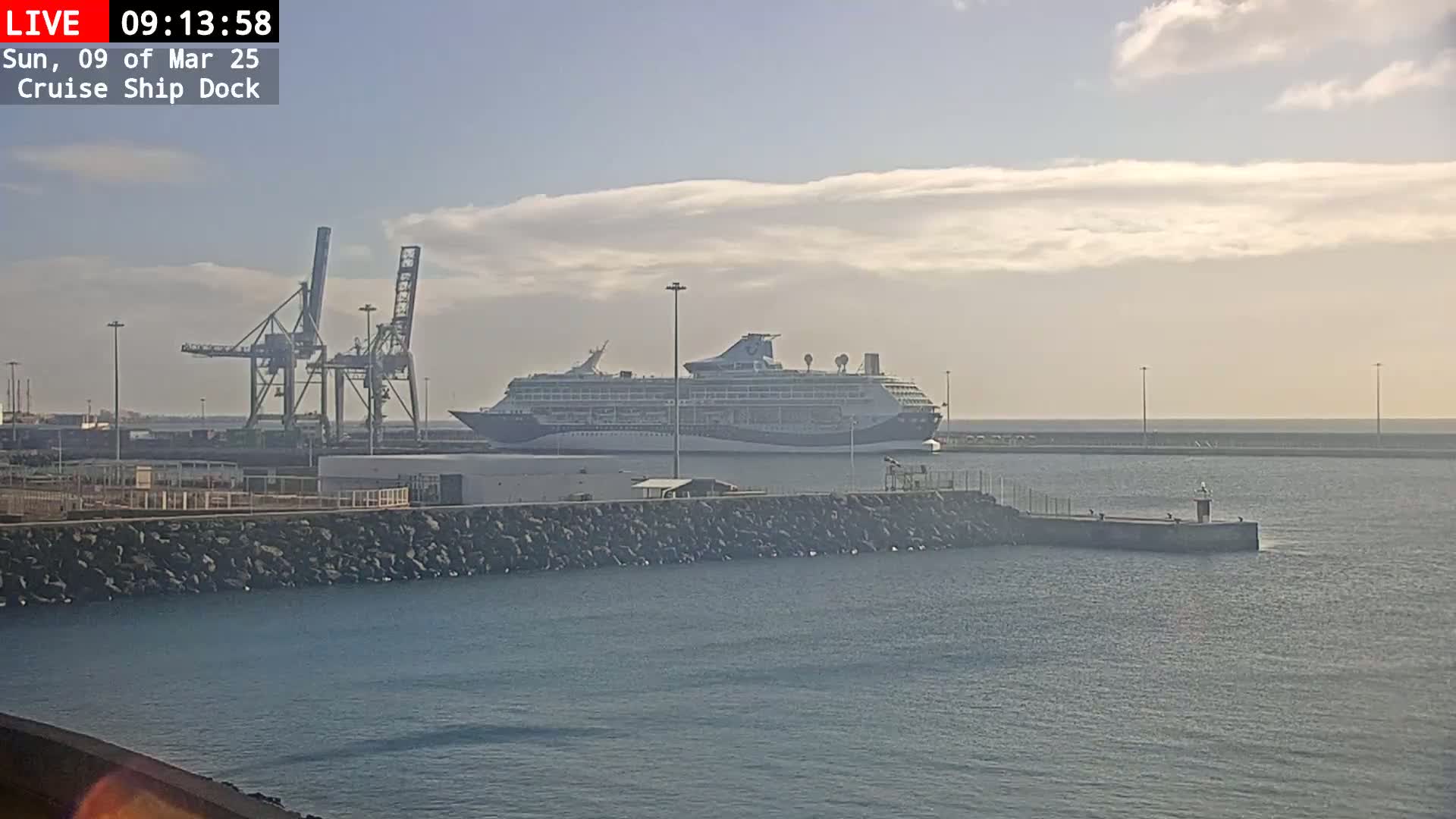 A large cruise ship is docked at a port under a partly cloudy sky.