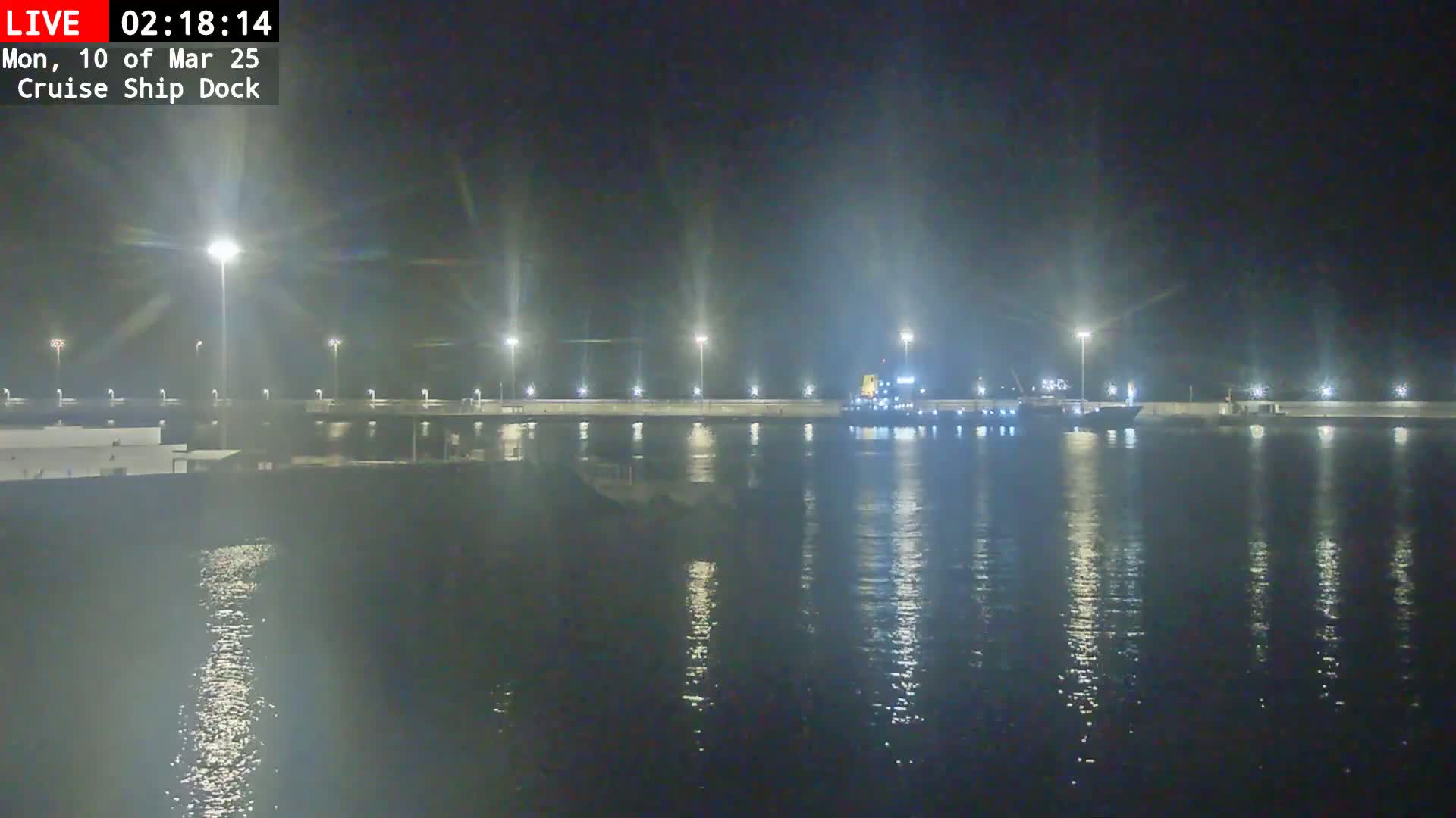 A cruise ship is docked at night next to a brightly lit pier, the water is calm and reflects the lights.