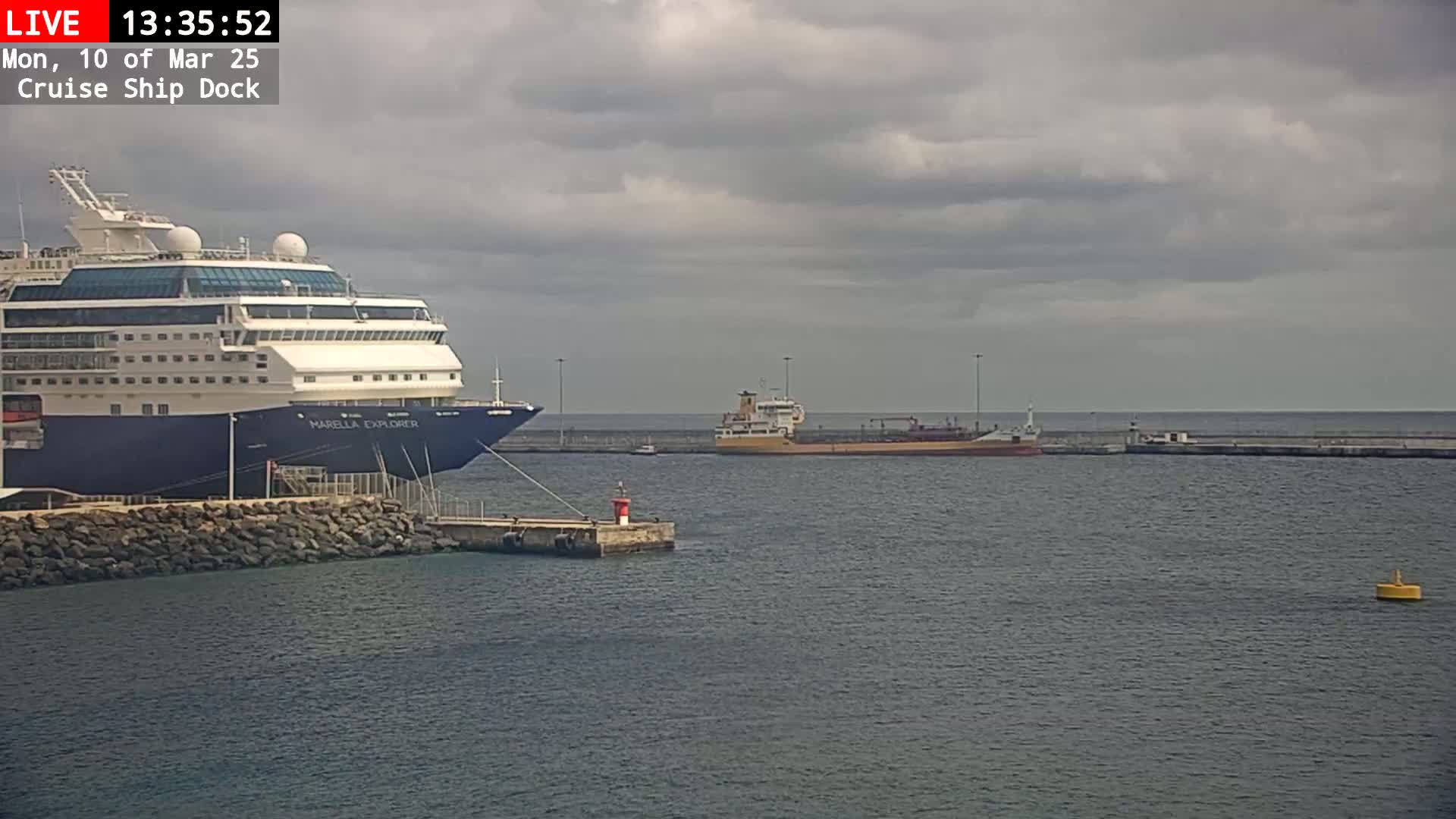 A large cruise ship is docked next to a smaller tanker in a harbor under a cloudy sky.