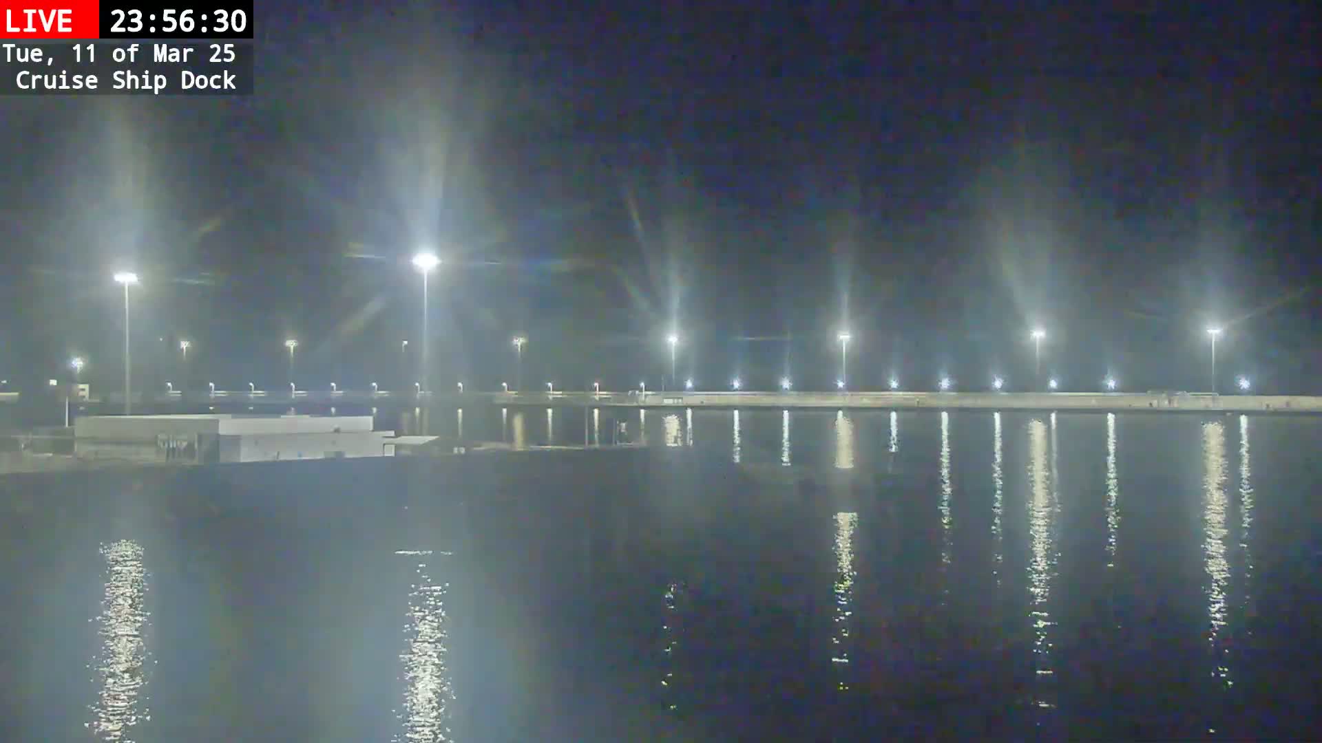 A brightly lit cruise ship dock at night is reflected in calm water.