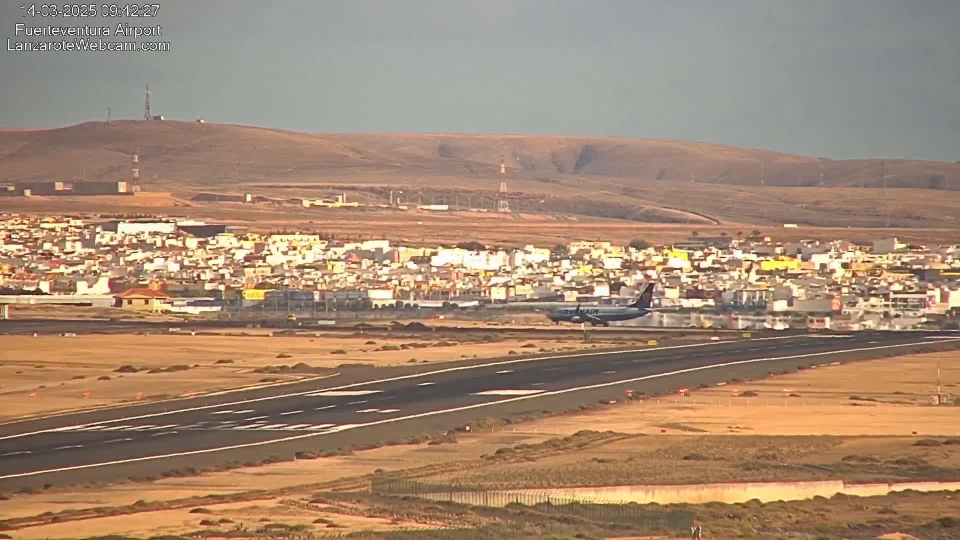 A passenger plane lands on a runway near a town under a hazy sky.