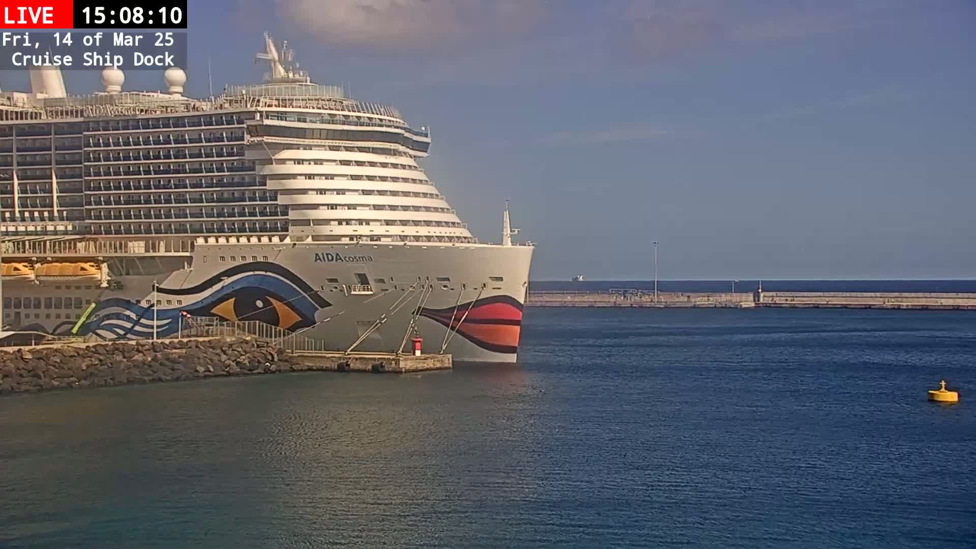 A large cruise ship is docked at a pier on a sunny day with calm water.