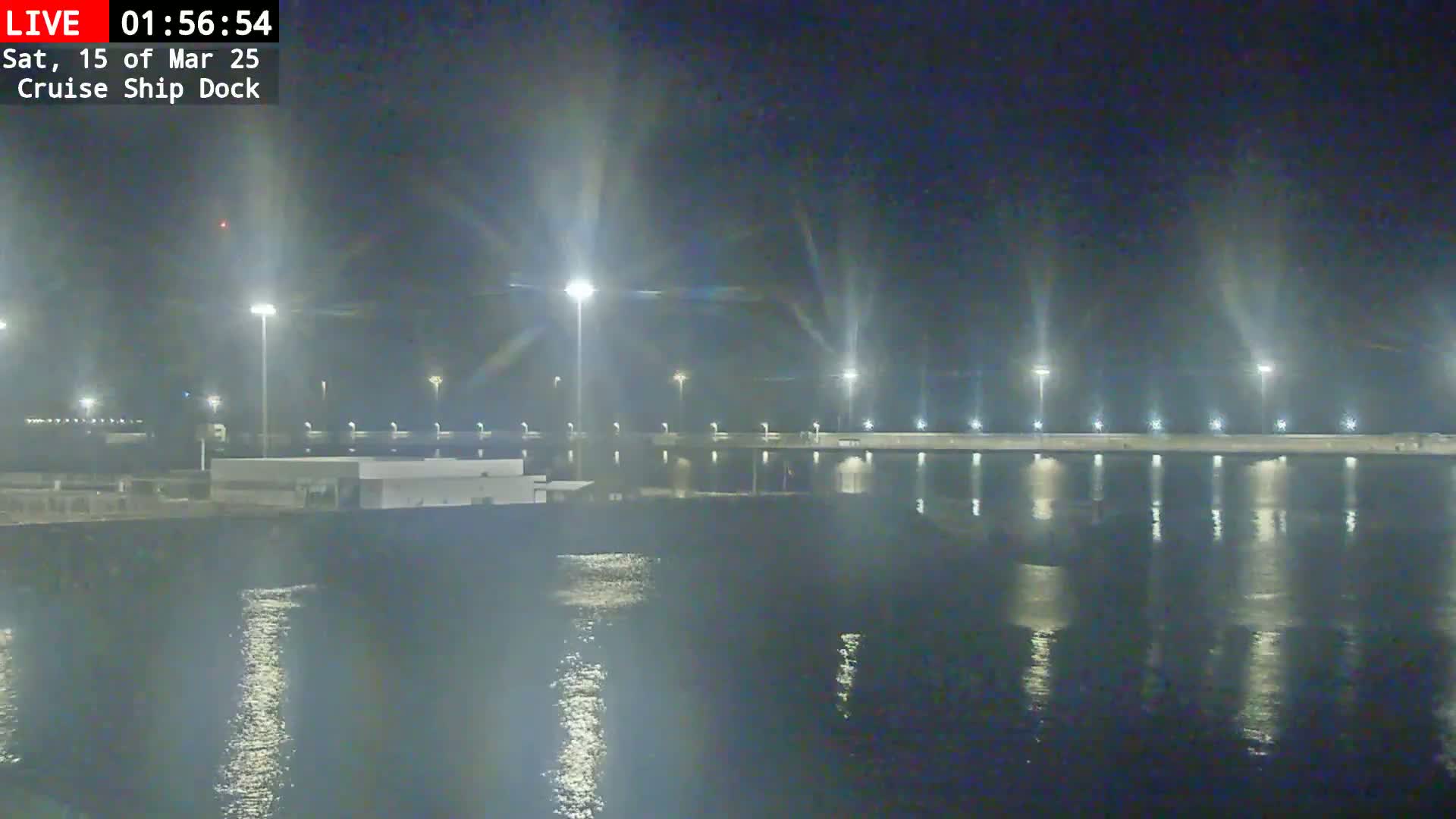 A nighttime view of a brightly lit cruise ship dock reflecting in calm water.