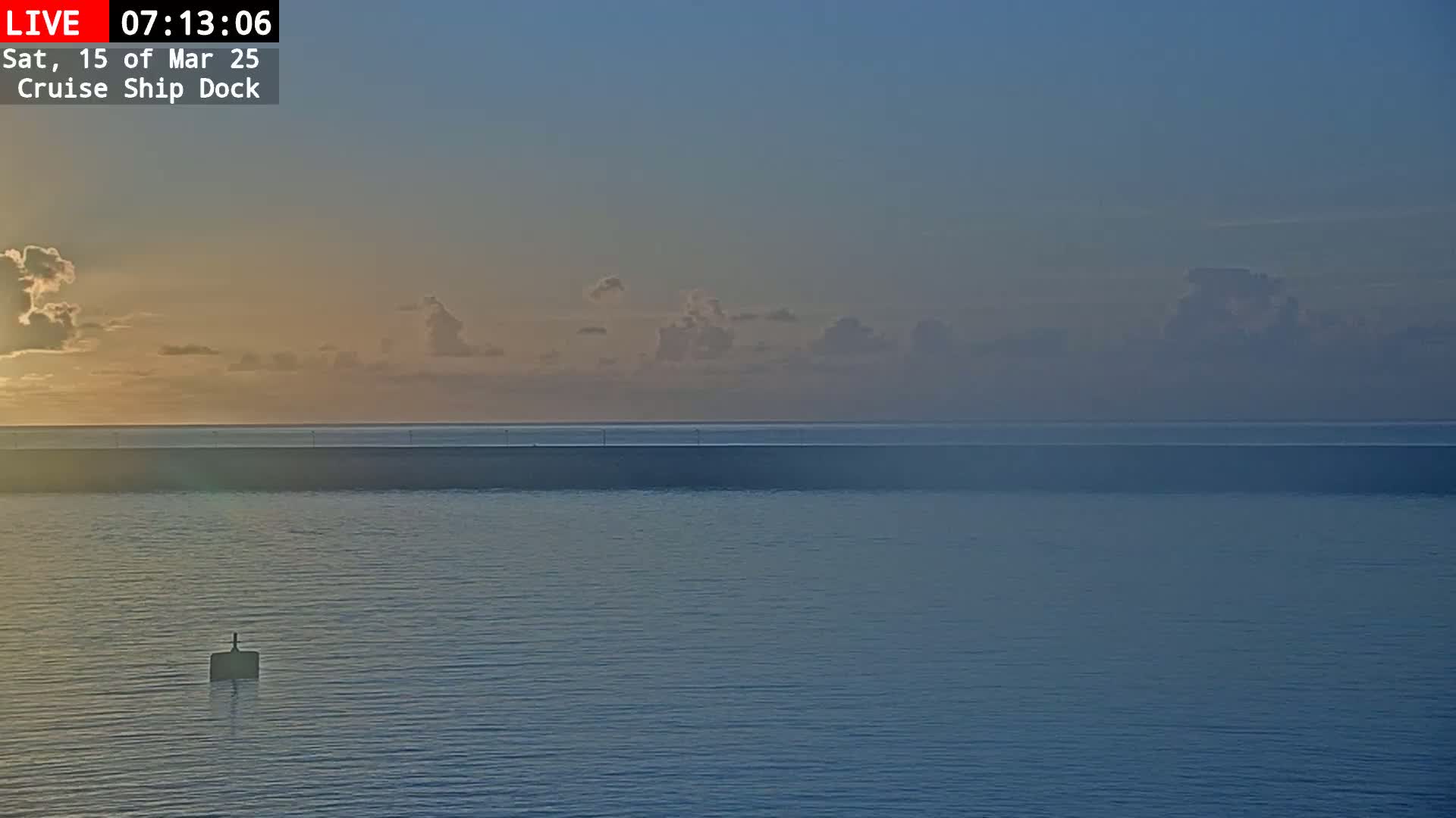 A calm body of water at sunrise, with a few clouds in a pale sky.