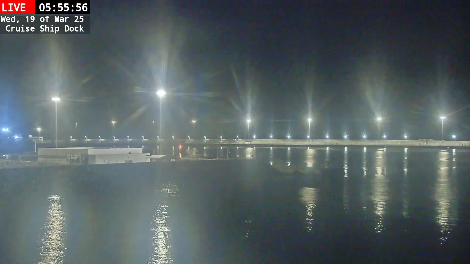 A brightly lit cruise ship dock at night reflects on calm water.