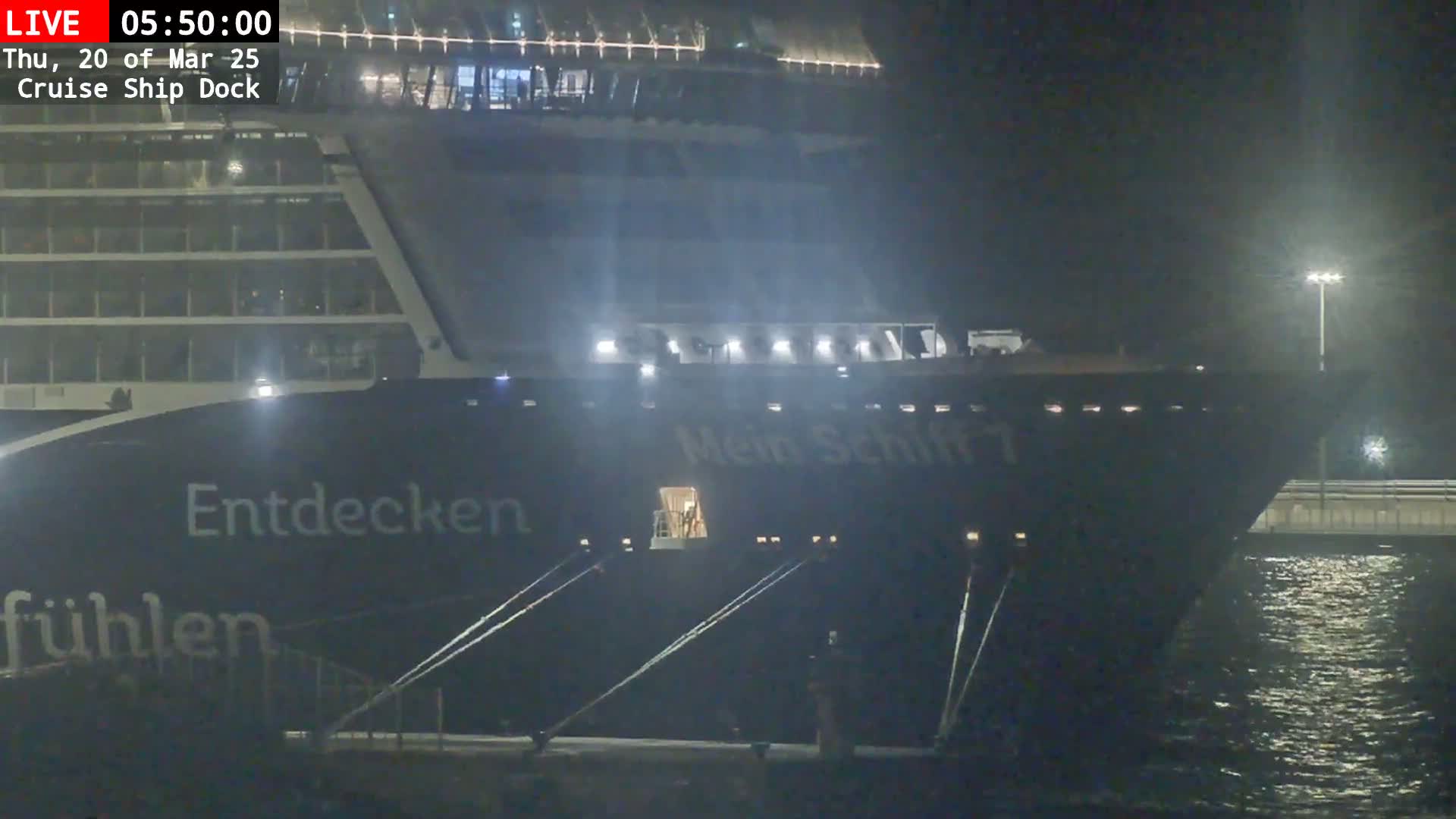 A large cruise ship is docked at night, illuminated by lights on the ship and dock.