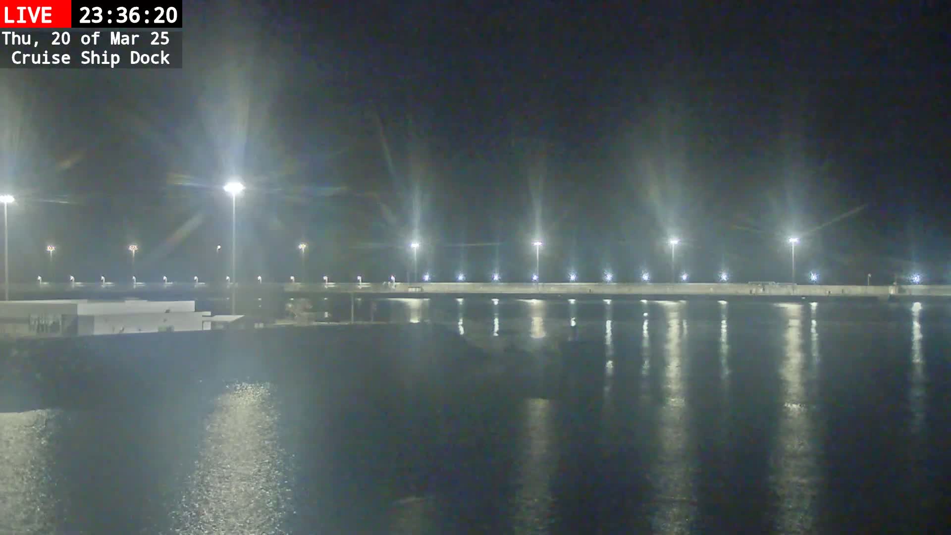 A nighttime view of a brightly lit cruise ship dock reflecting in calm water.