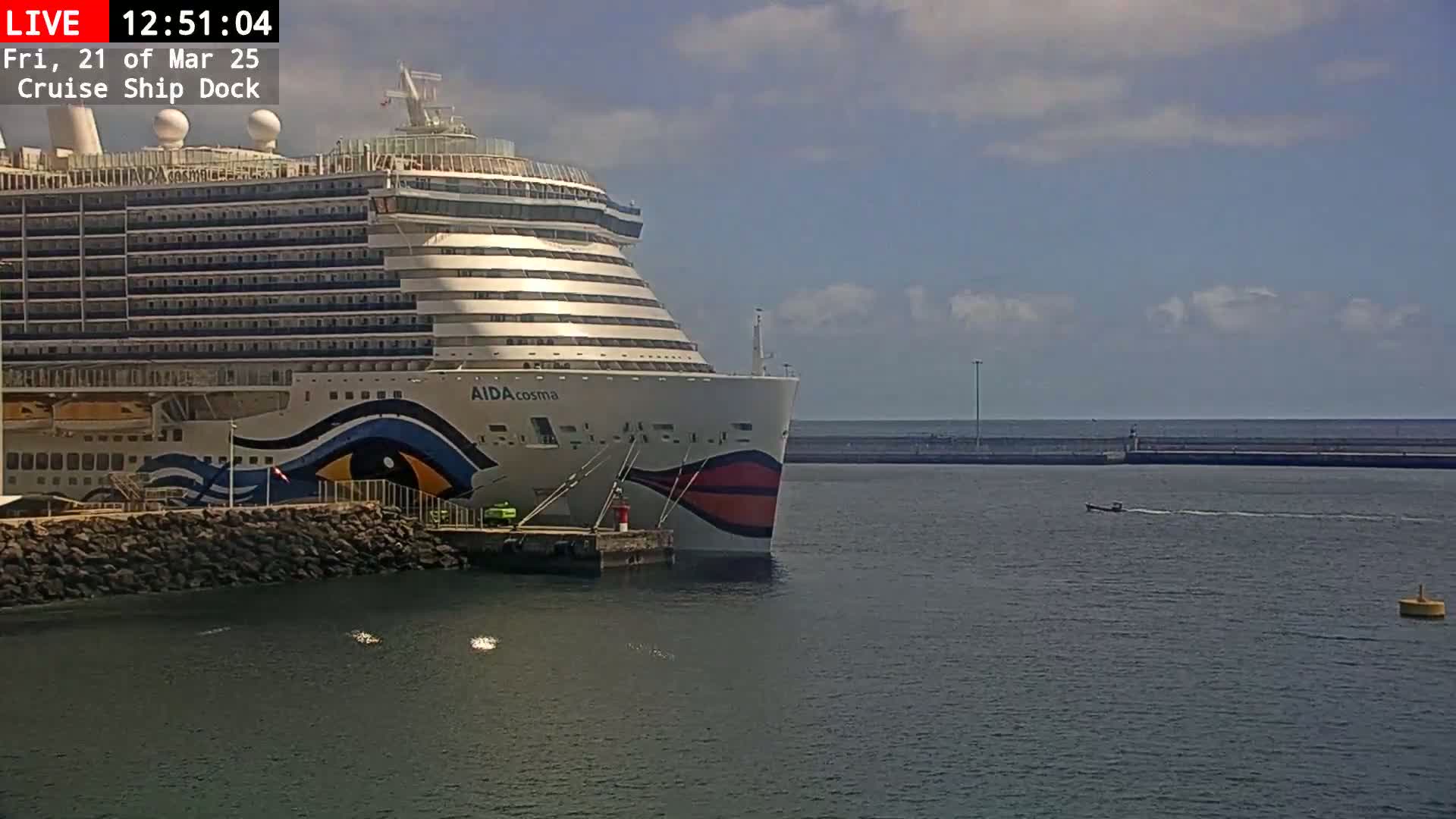 A large cruise ship is docked at a port on a partly cloudy day.
