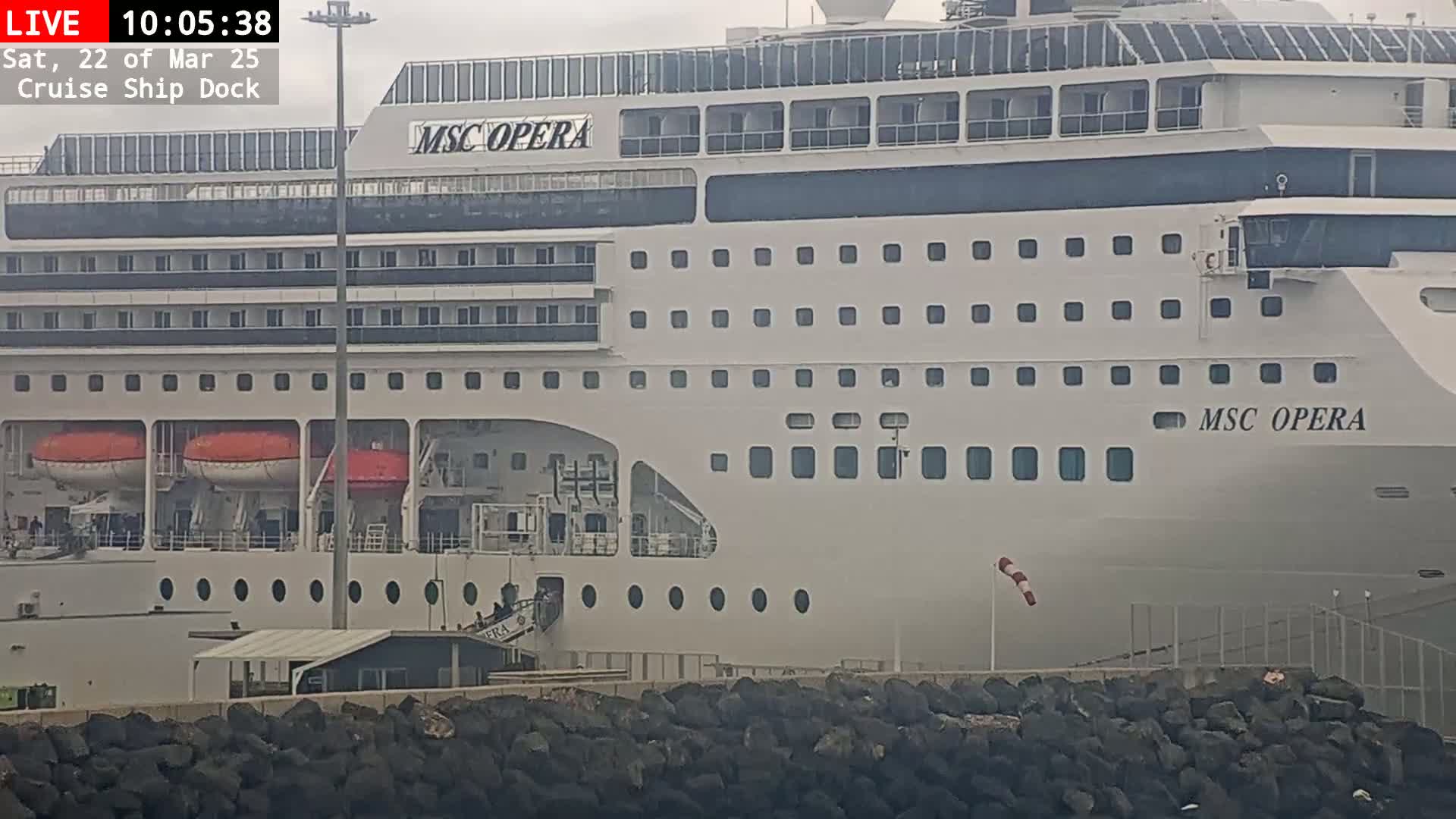 A large cruise ship, the MSC Opera, is docked at a port on an overcast day.