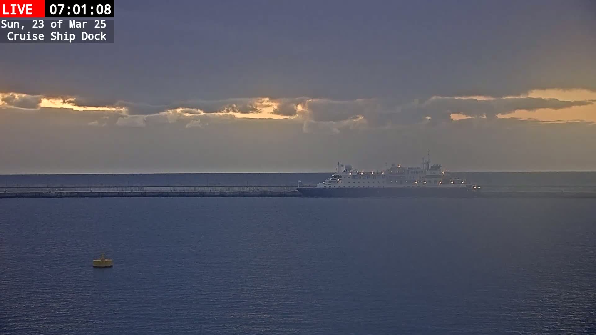 A large cruise ship is docked at a pier under a partly cloudy sunrise sky.