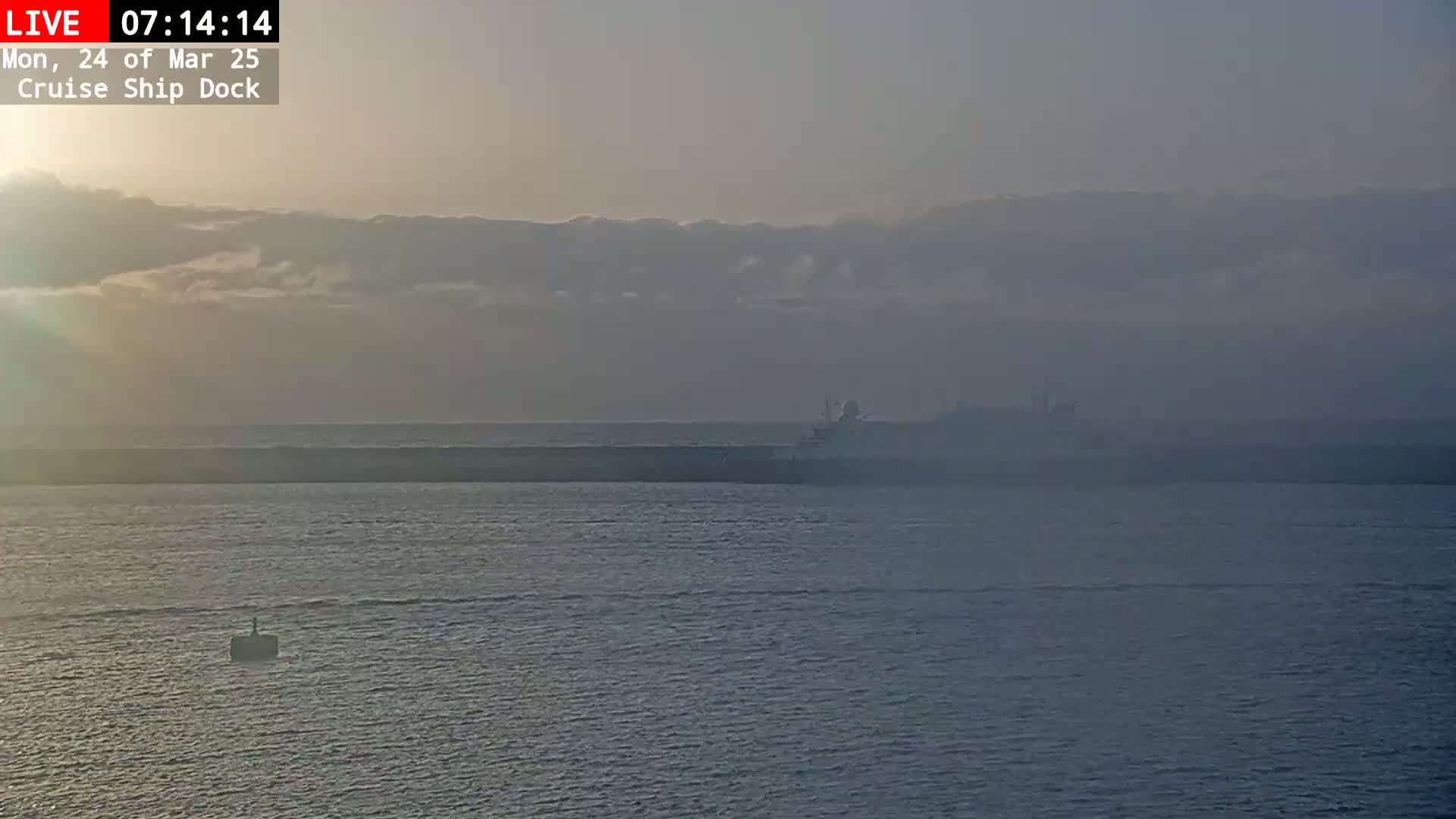 A cruise ship is visible in the distance on a hazy, calm body of water at sunrise.