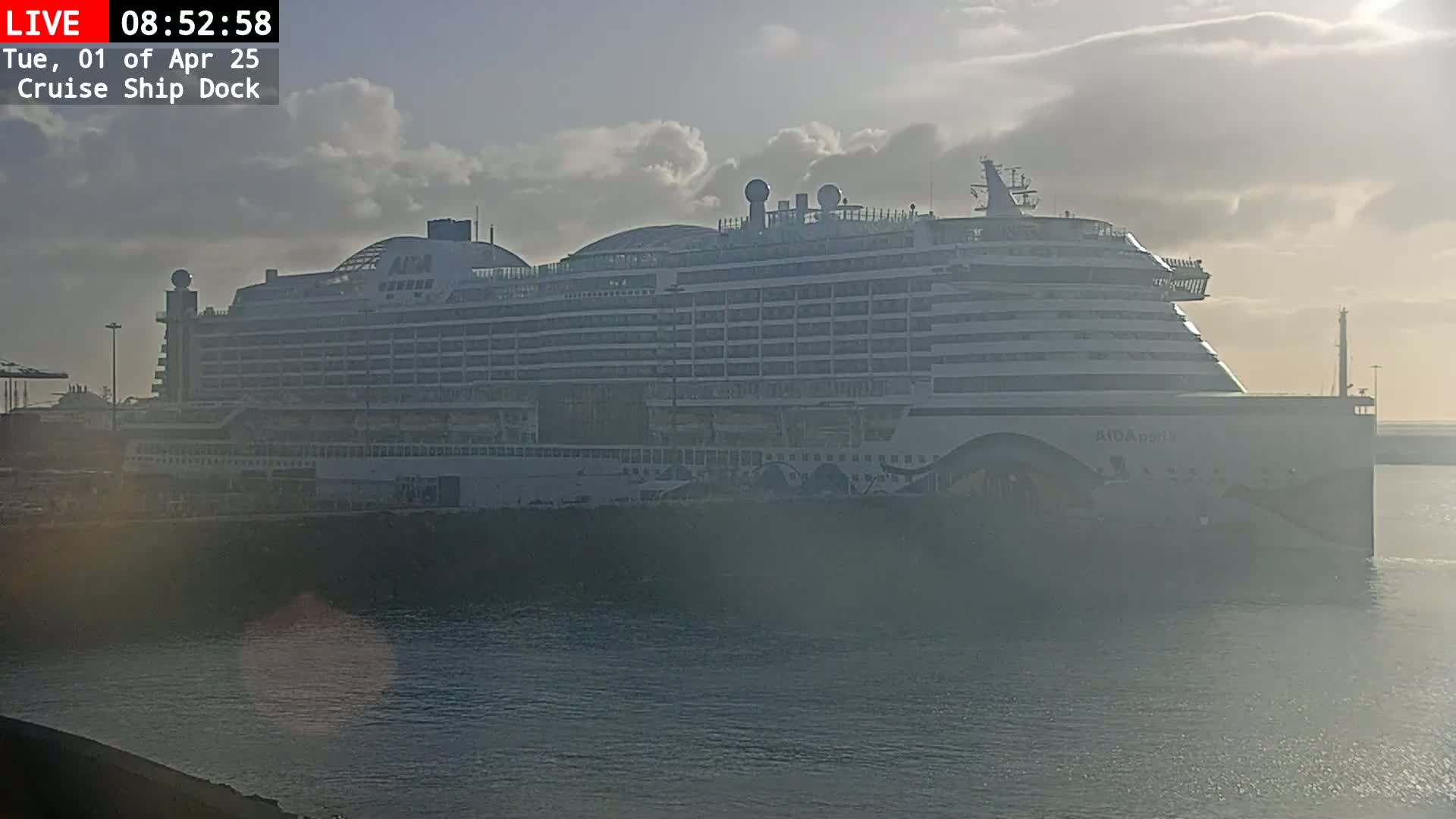 A large cruise ship is docked at a port under a partly cloudy sky.