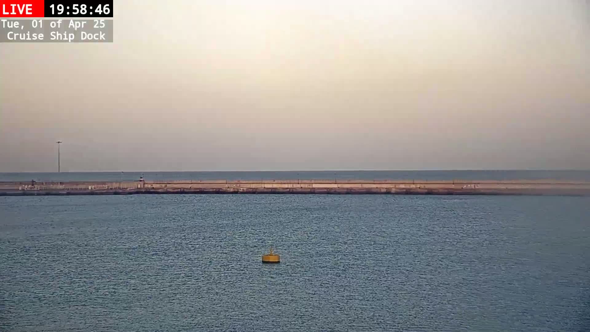 A long, low pier extends into a calm, hazy sea under a pale sky.