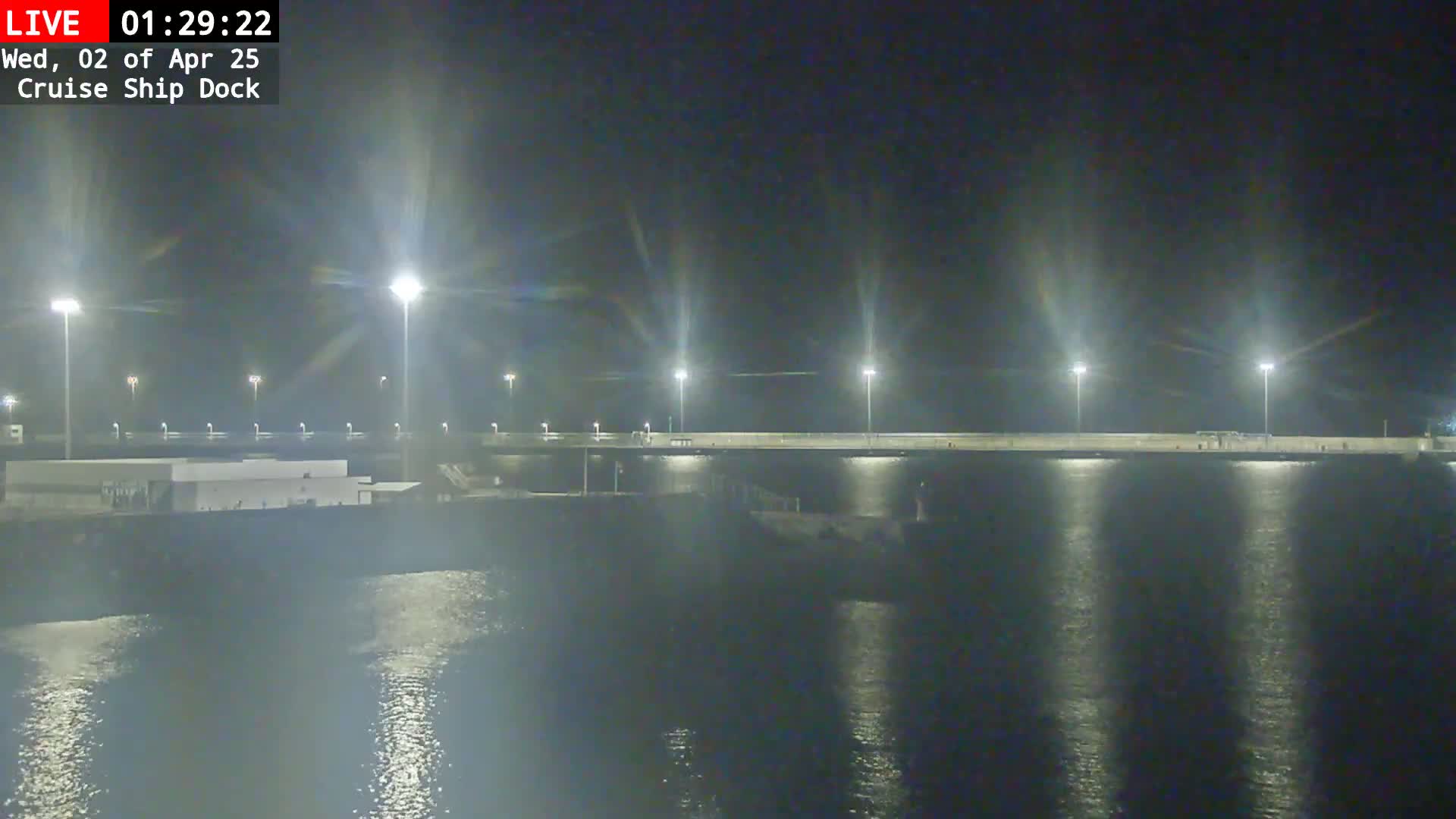 A nighttime view of a cruise ship dock illuminated by bright lights, reflecting on calm water.