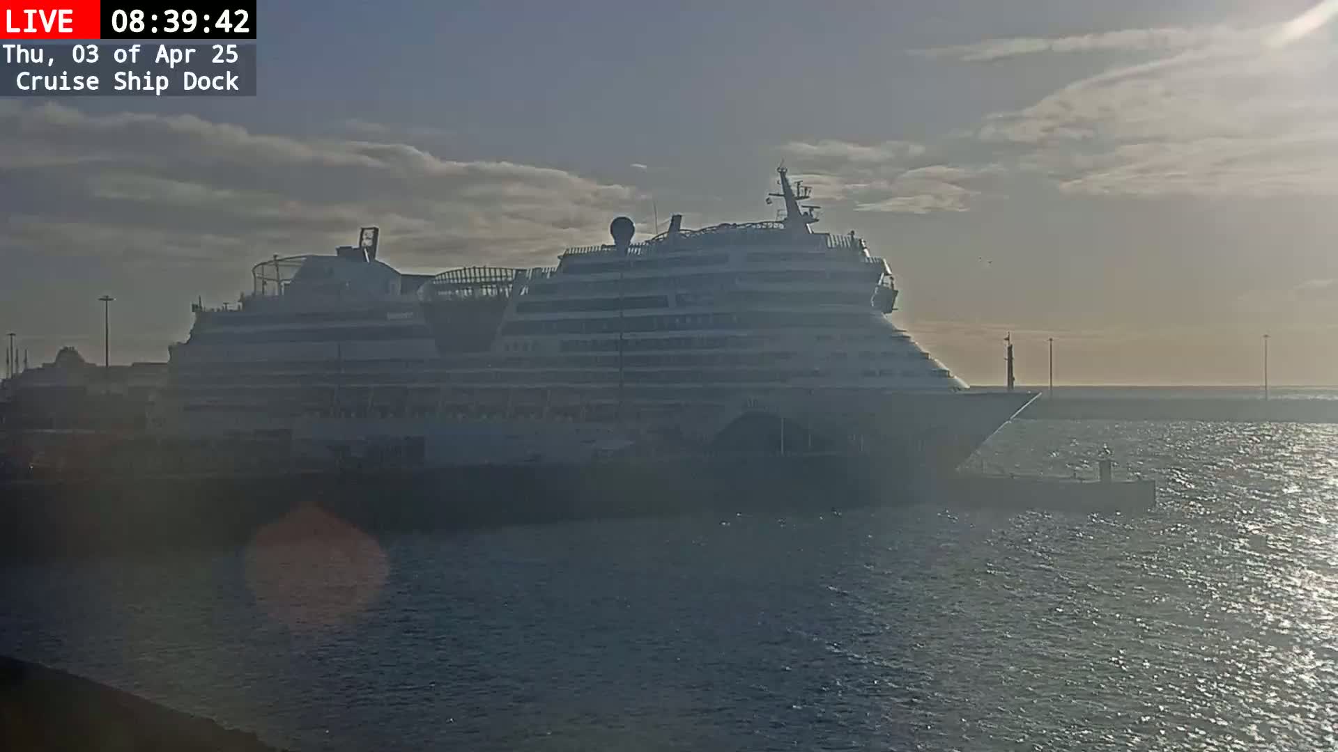 A large cruise ship is docked at a port on a cloudy but bright day.