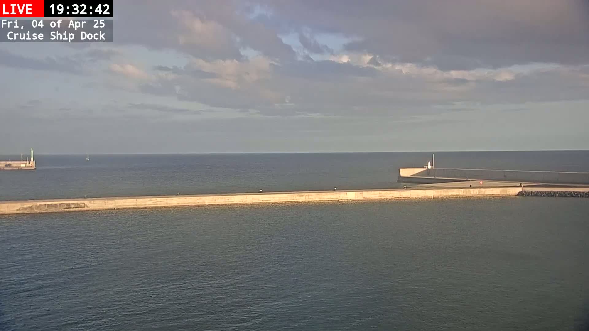 A long concrete pier extends into a calm sea under a partly cloudy sky.