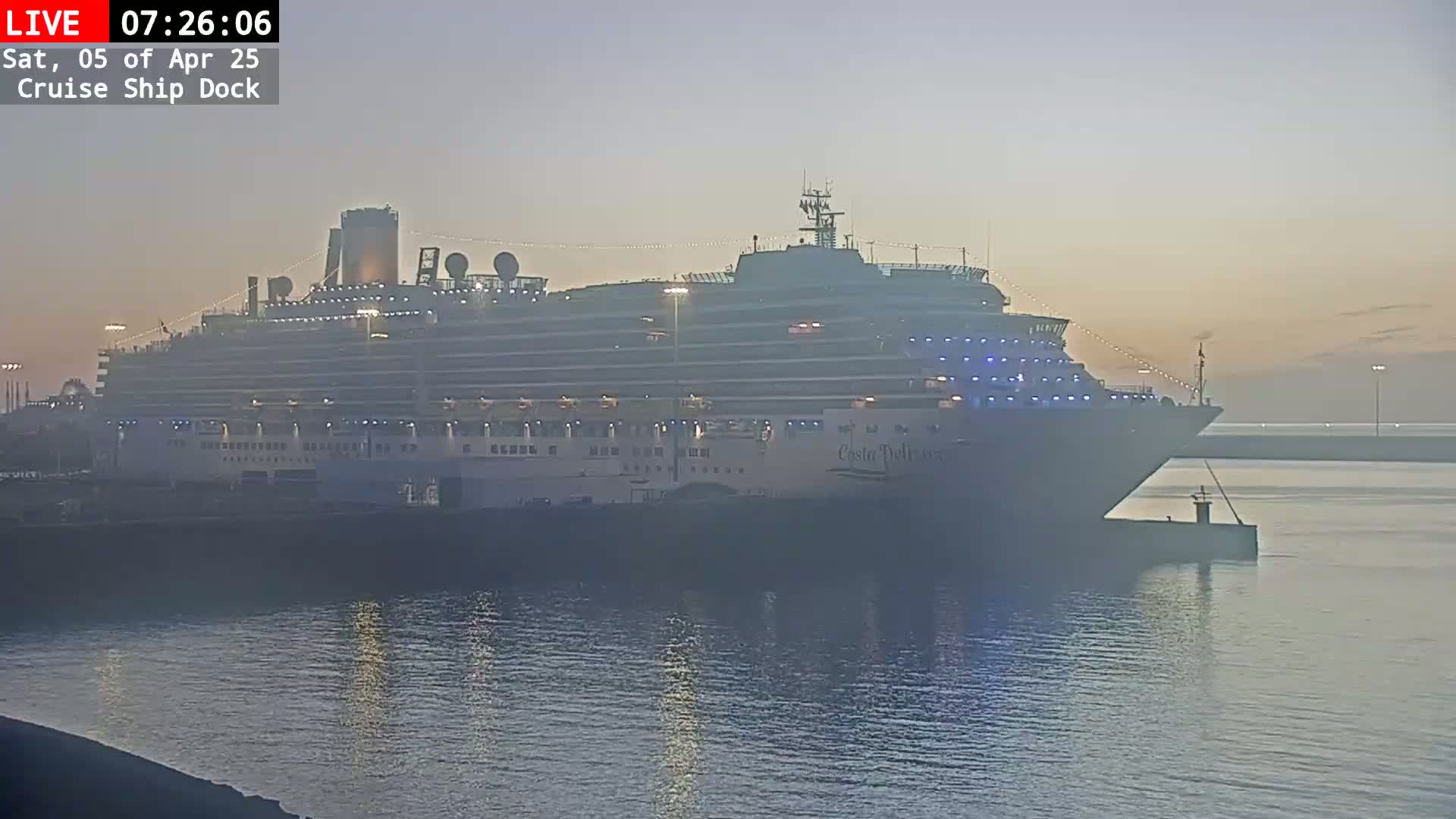 A large cruise ship is docked at a pier in hazy, dawn-like conditions.