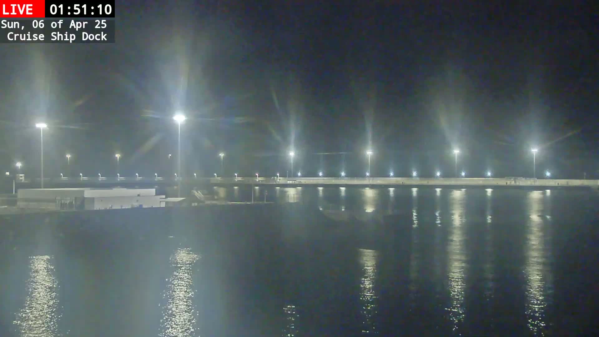 A brightly lit cruise ship dock at night is reflected in the calm water.