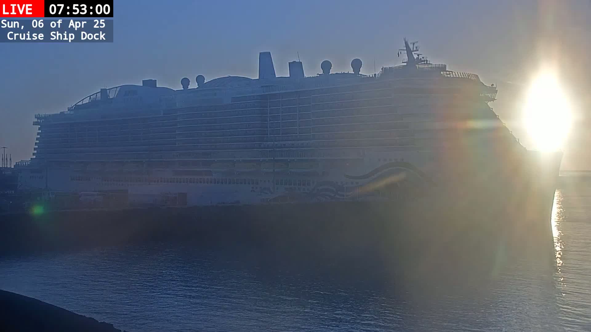 A large cruise ship is docked at sunrise in calm water.